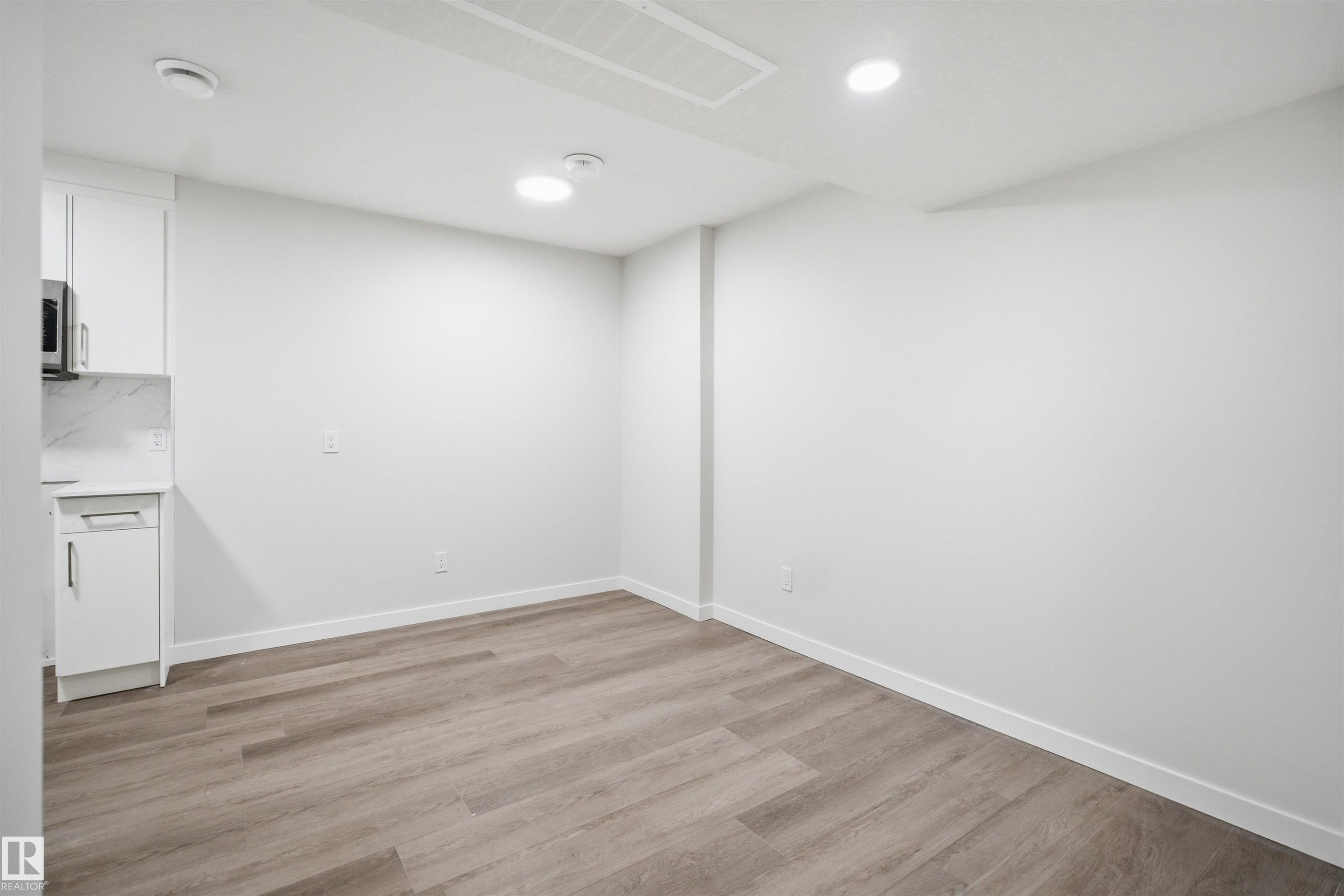 This bright interior space features light-colored walls and wood-style flooring, complemented by white baseboards - 2125 Maple Road Nw, Edmonton, AB - Indoor Photo Showing Other Room