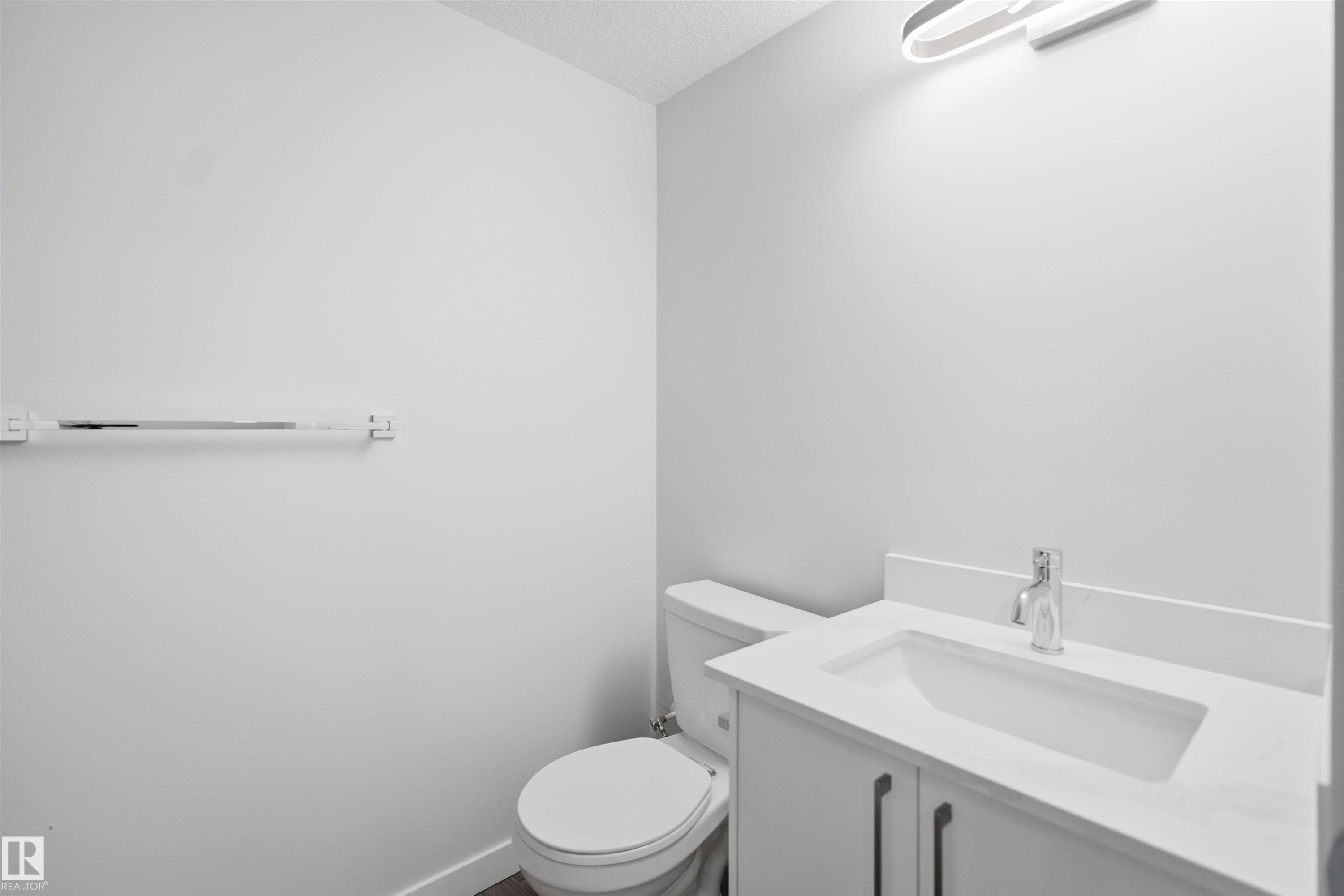 This bathroom features a contemporary vanity with a white countertop and a chrome faucet, a white toilet, and a towel bar mounted on a white wall - 2125 Maple Road Nw, Edmonton, AB - Indoor Photo Showing Bathroom