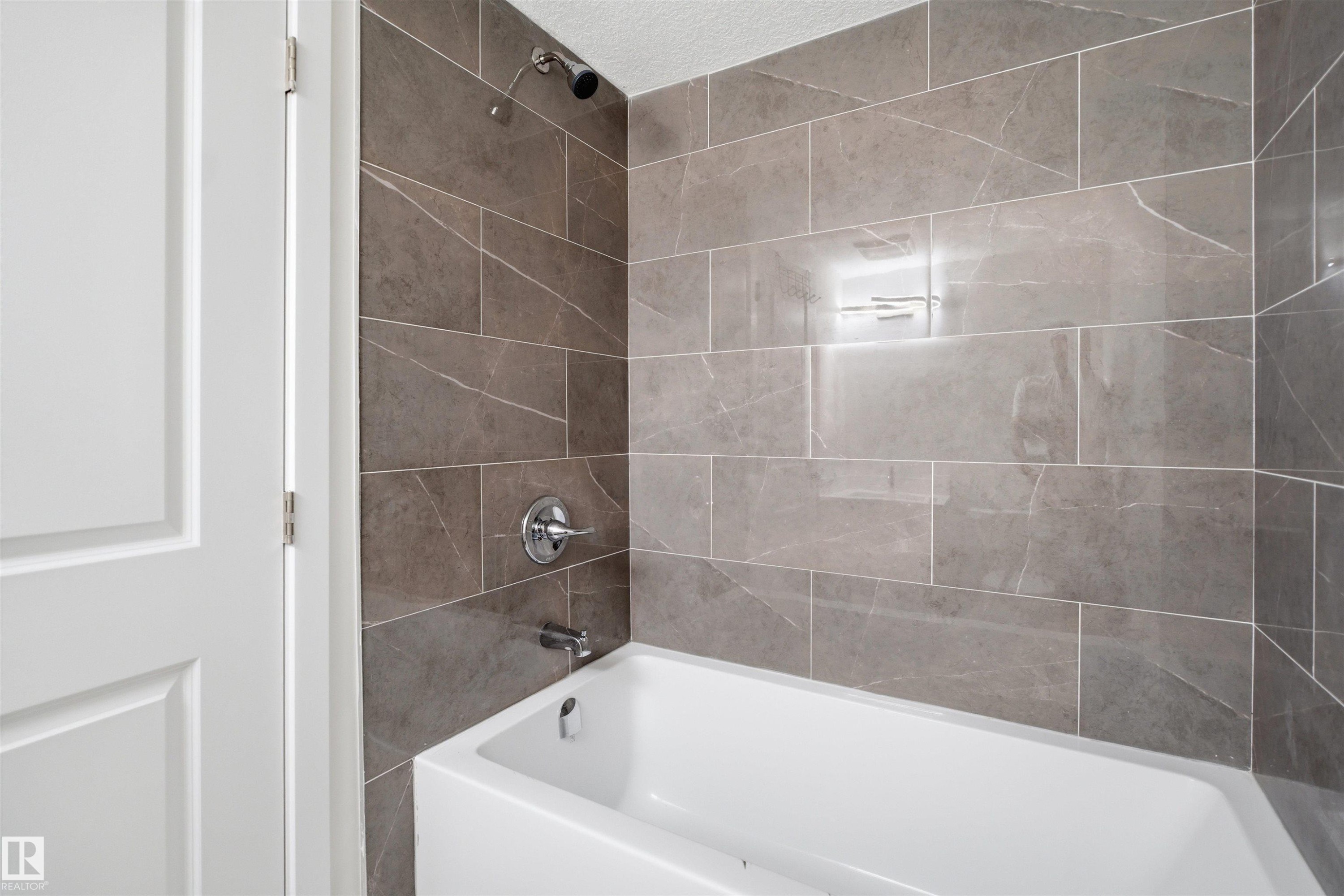 The bathroom features a white bathtub with chrome fixtures and gray rectangular wall tiles - 2125 Maple Road Nw, Edmonton, AB - Indoor Photo Showing Bathroom