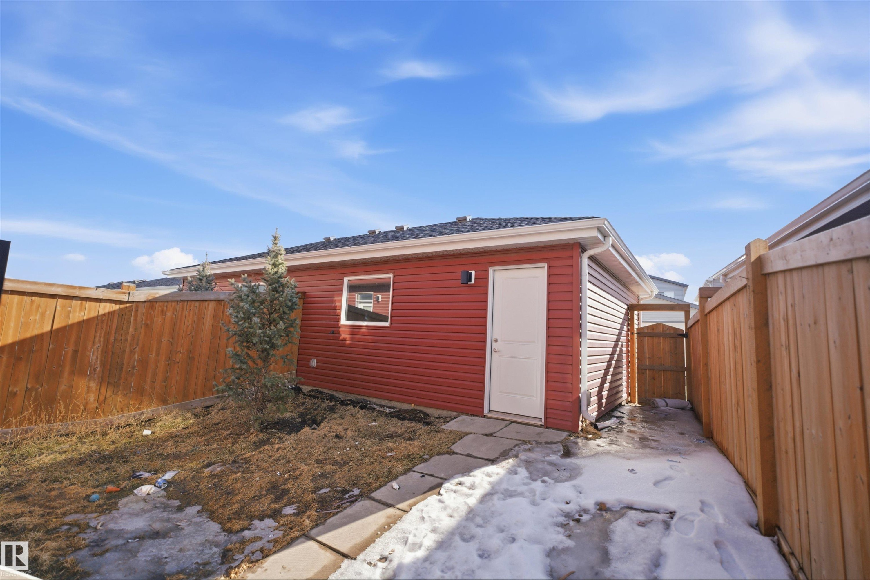 The property includes an exterior building with red siding, a white door, and a small window, set within a fenced yard - 2125 Maple Road Nw, Edmonton, AB - Outdoor