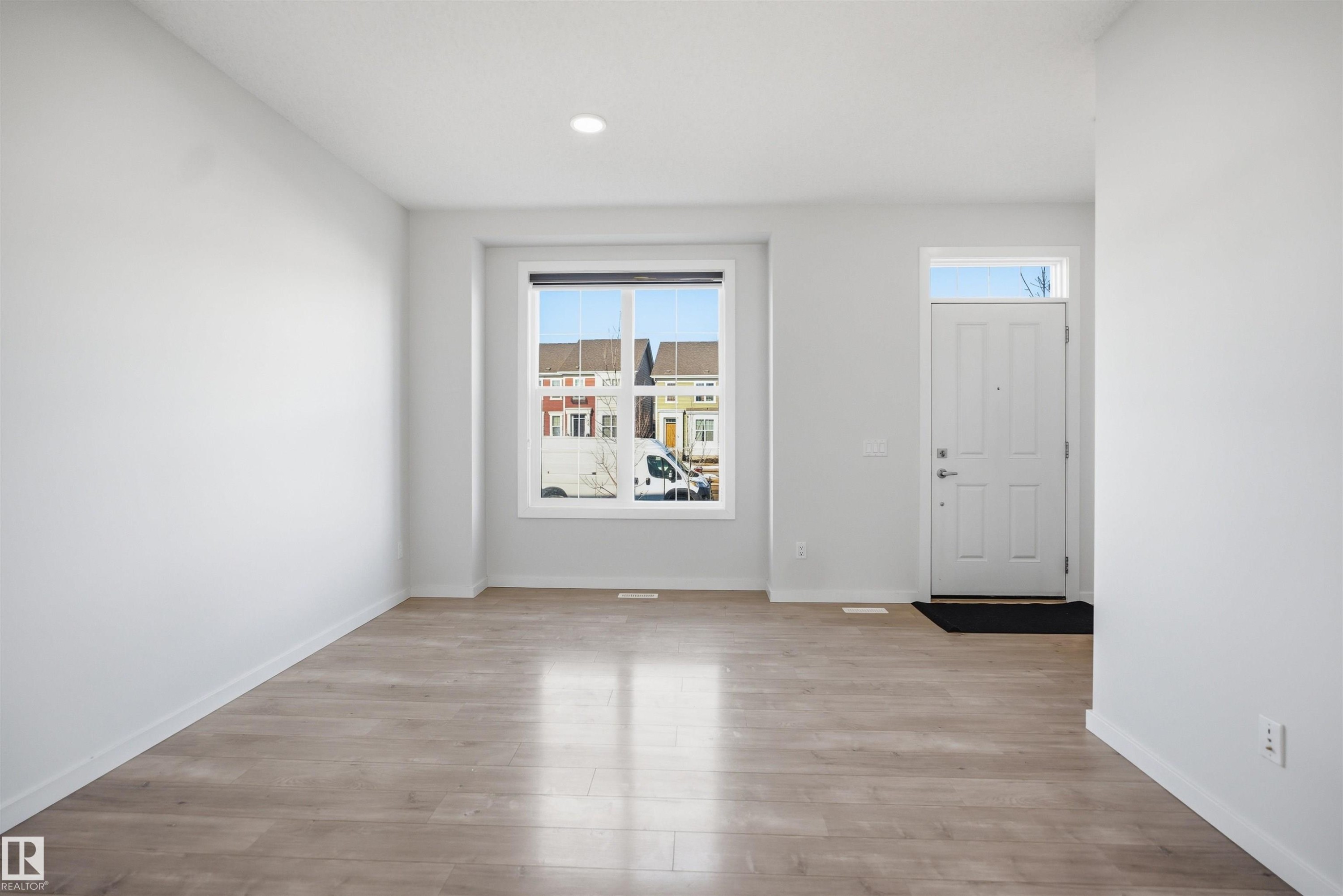 This bright interior space features light-toned flooring, a window offering views of the surrounding neighborhood, and a white entry door with a transom window - 2125 Maple Road Nw, Edmonton, AB - Indoor Photo Showing Other Room
