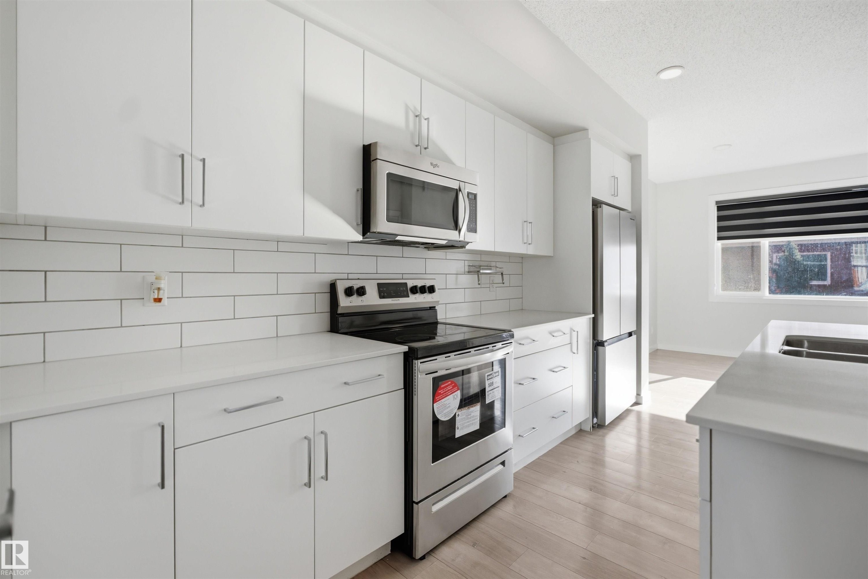 Well-appointed kitchen featuring white cabinetry, white subway tile backsplash, and stainless steel appliances including a range, microwave, and refrigerator - 2125 Maple Road Nw, Edmonton, AB - Indoor Photo Showing Kitchen With Stainless Steel Kitchen With Double Sink With Upgraded Kitchen