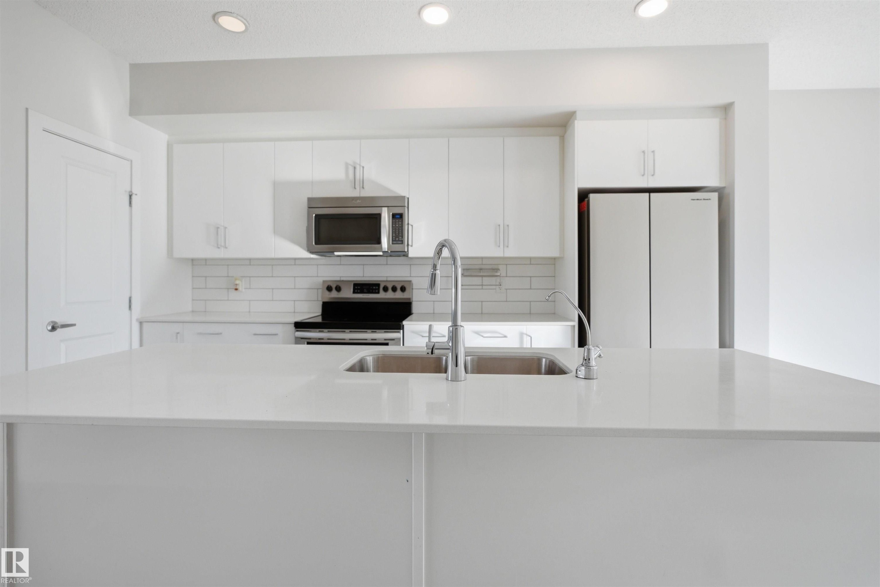 Modern kitchen with white cabinetry, stainless steel microwave, and white subway tile backsplash - 2125 Maple Road Nw, Edmonton, AB - Indoor Photo Showing Kitchen With Double Sink With Upgraded Kitchen