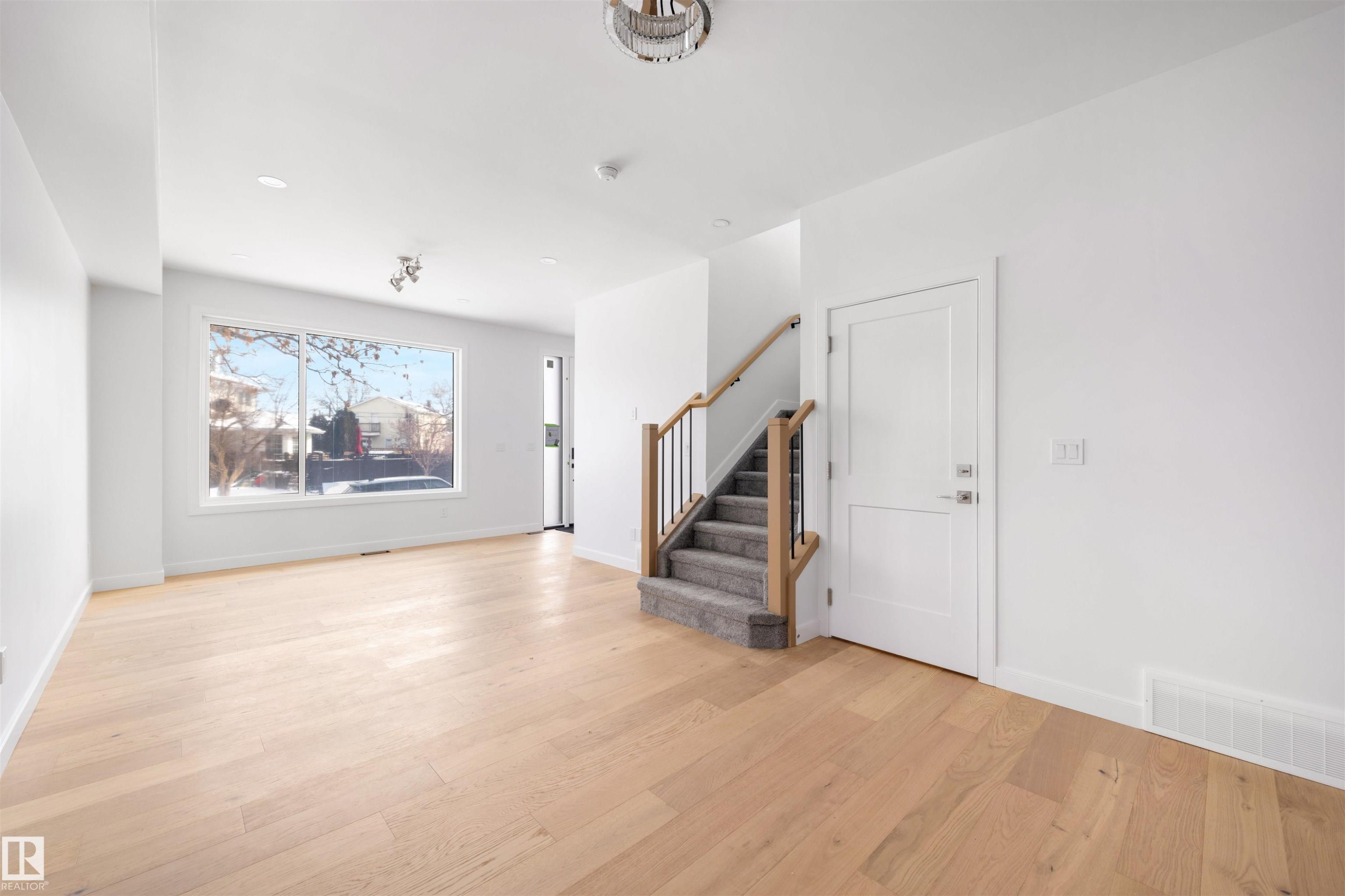 Inviting main living area featuring light wood flooring, a large window, and a staircase with a wood handrail and black balusters - 7927 112S Avenue, Edmonton, AB - Indoor