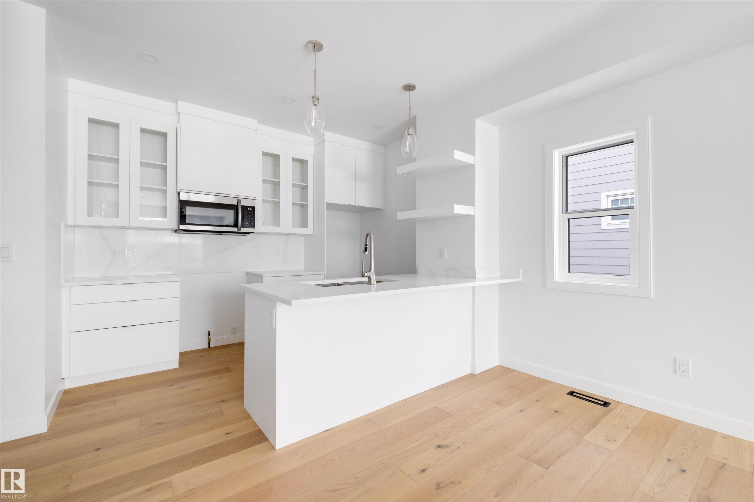 The kitchen features a white island with a sink, white cabinetry, and a microwave - 7927 112S Avenue, Edmonton, AB - Indoor Photo Showing Kitchen