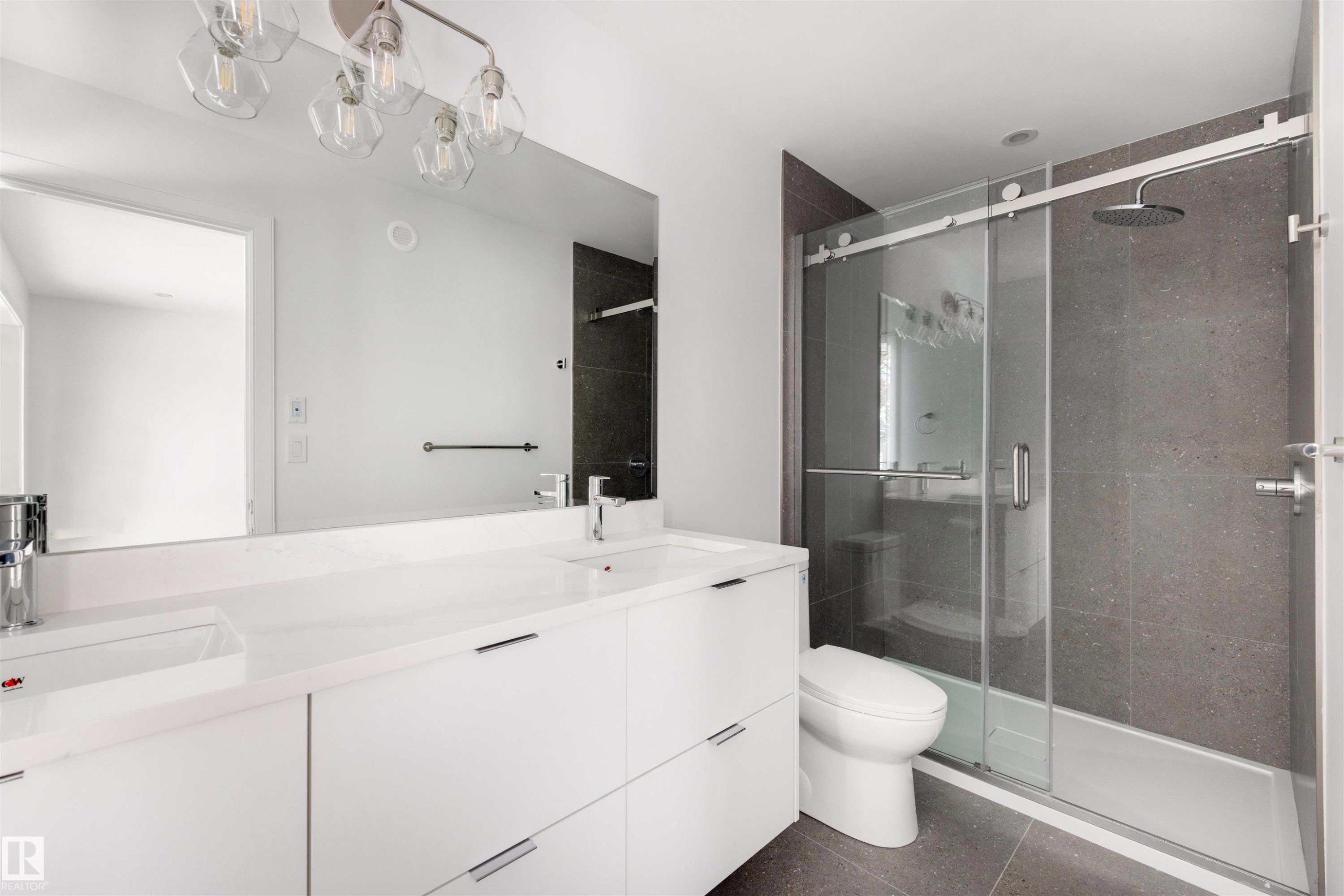 Bathroom featuring a spacious double vanity with white cabinets, a large mirror, and an enclosed shower with dark tile surround and a rain shower head - 7927 112S Avenue, Edmonton, AB - Indoor Photo Showing Bathroom
