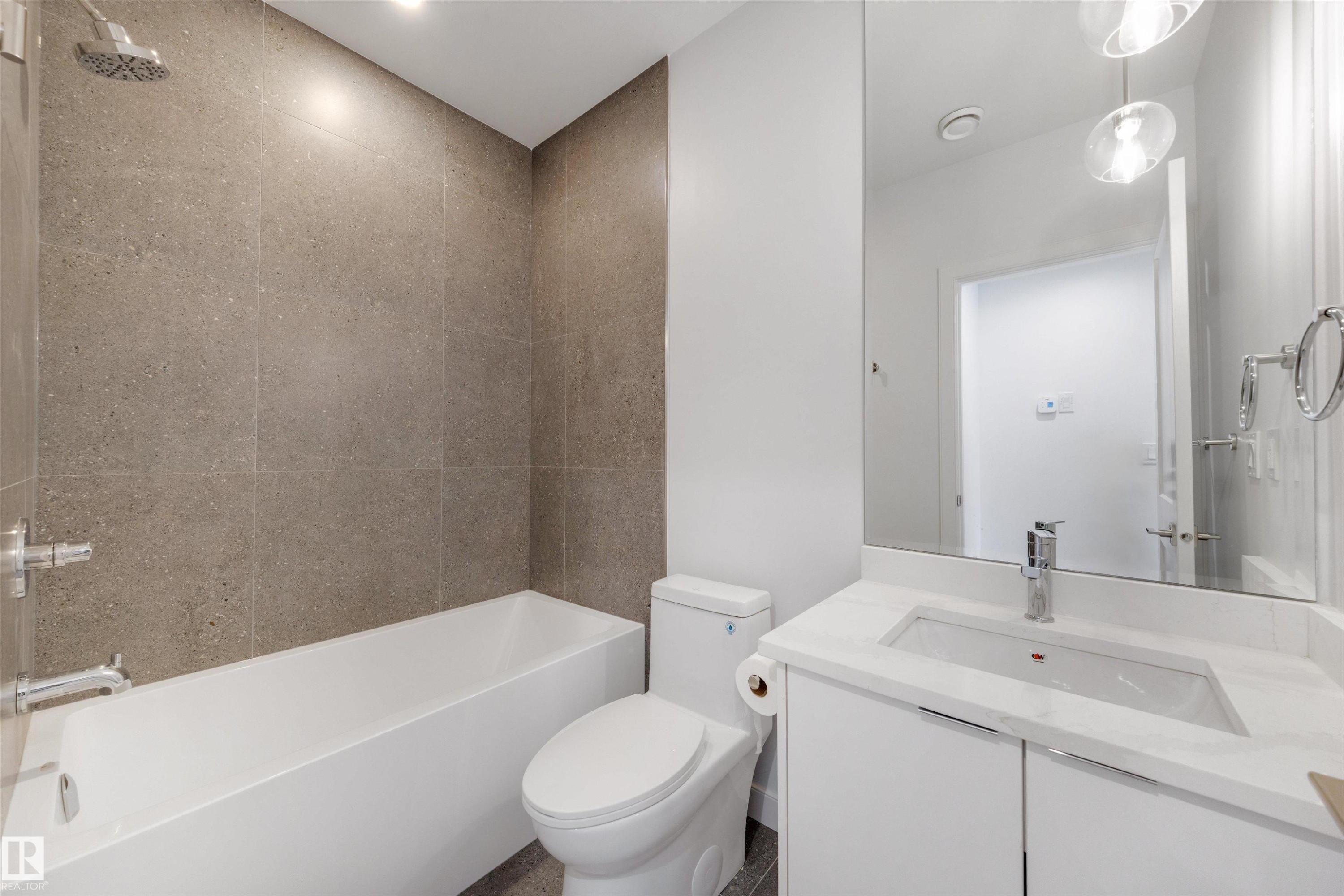 Bathroom with a white bathtub, a toilet, a vanity with a white countertop and integrated sink, a large mirror, and tiled walls in the shower area - 7927 112S Avenue, Edmonton, AB - Indoor Photo Showing Bathroom
