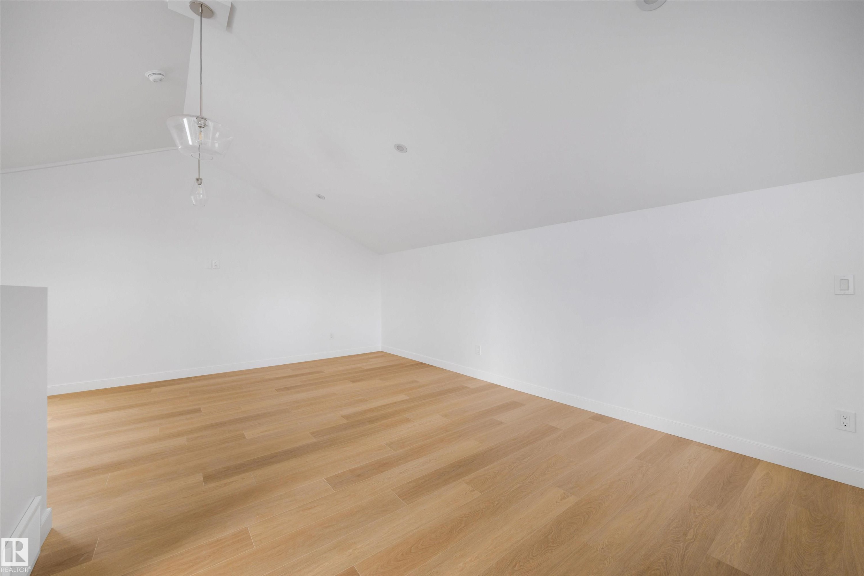 This expansive room features light hardwood flooring, crisp white walls, and a vaulted ceiling with a modern pendant light fixture and recessed lighting - 7927 112S Avenue, Edmonton, AB - Indoor Photo Showing Other Room