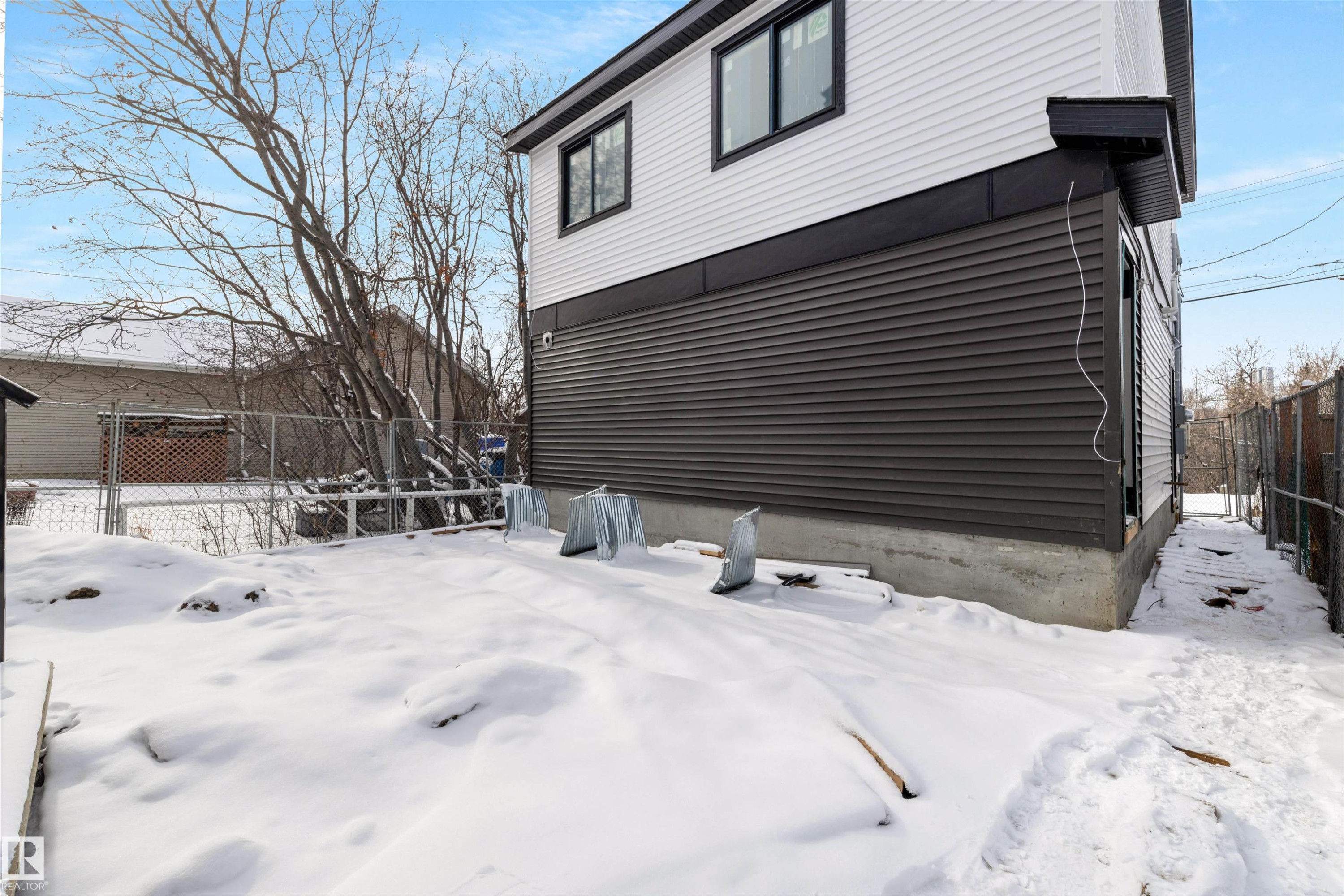 The property features white and dark gray horizontal siding, black trim around the windows, and a concrete foundation - 7927 112S Avenue, Edmonton, AB - Outdoor With Exterior