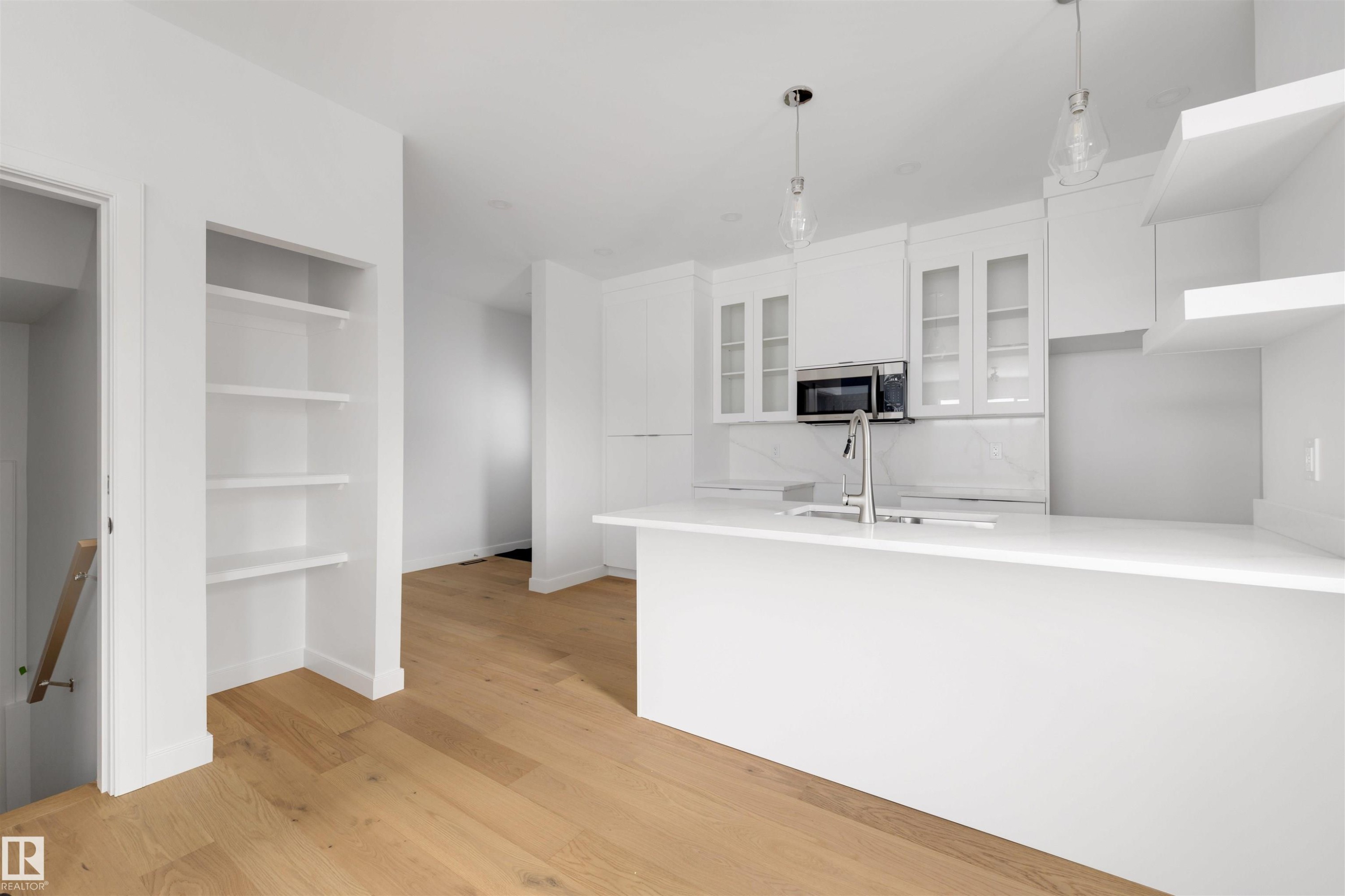 Open concept kitchen and living area featuring light wood flooring, white cabinetry, a kitchen island with an integrated sink, and stainless steel appliances - 7927 112S Avenue, Edmonton, AB - Indoor Photo Showing Kitchen With Double Sink