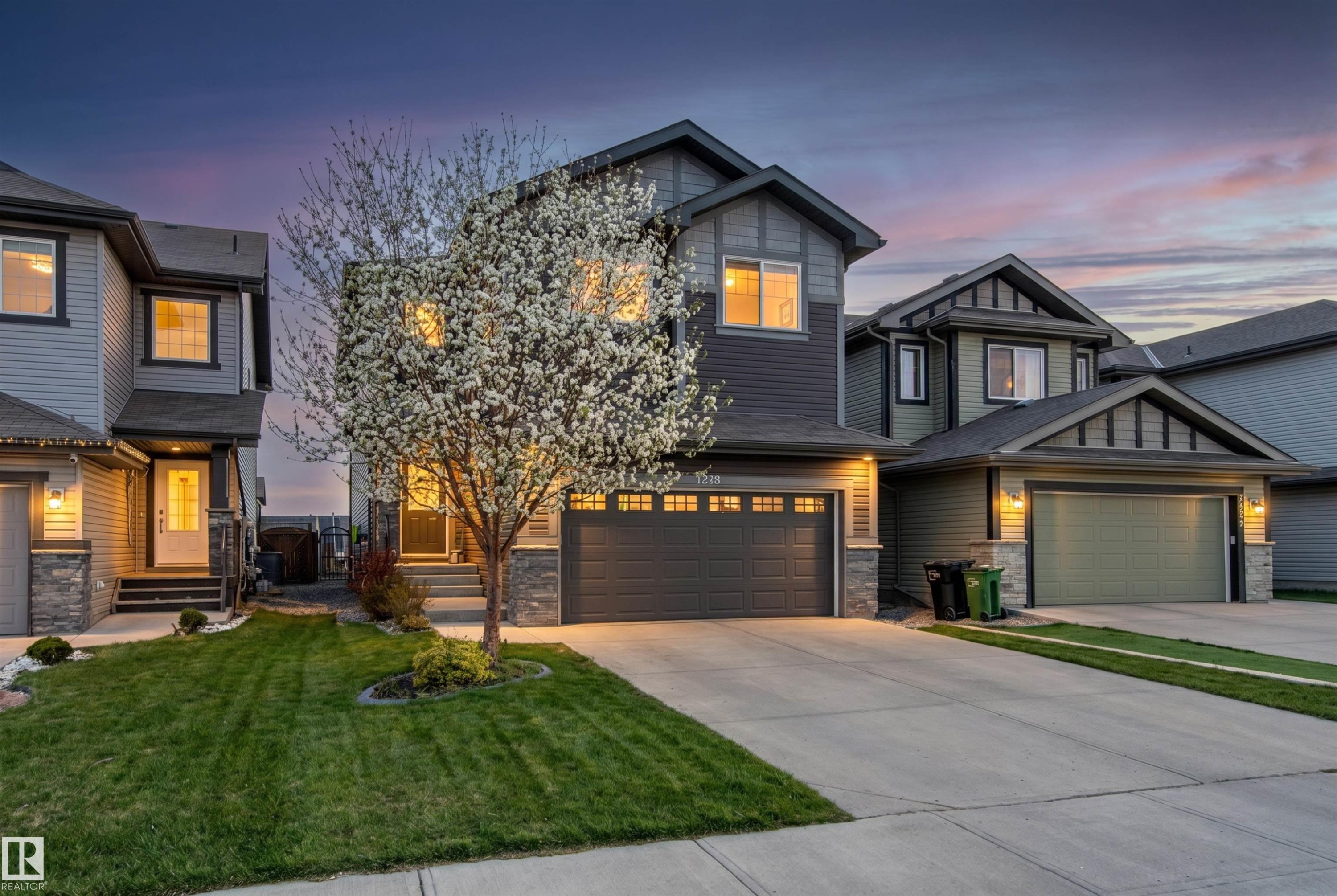 Two-story residence featuring a dark gray facade with stone accents and a prominent flowering tree - 7343 Armour Crescent, Edmonton, AB - Outdoor With Facade