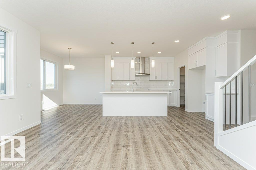 Open-concept living space featuring wood-finish flooring, white walls, and contemporary lighting fixtures - 6271 180 Avenue Nw, Edmonton, AB