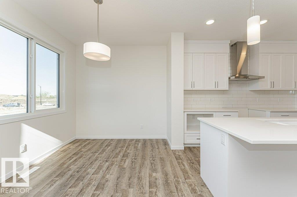 Open-concept living space featuring wood-finish flooring, a contemporary drum pendant light, and a large window - 6271 180 Avenue Nw, Edmonton, AB