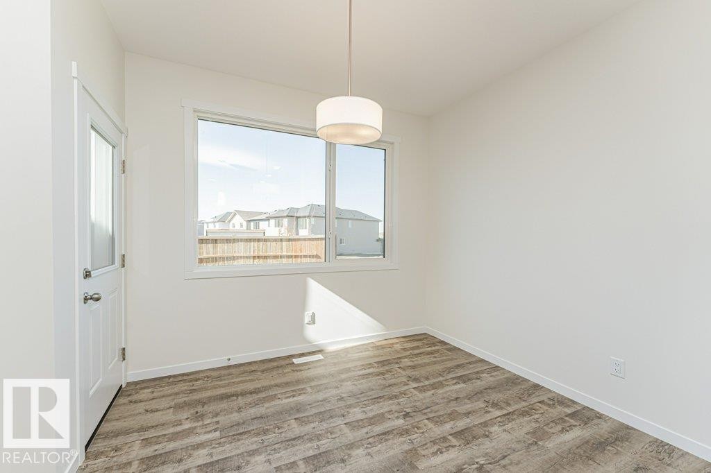 Bright interior space featuring a drum pendant light fixture, wood-finish flooring, white baseboards, and a window with white trim - 6271 180 Avenue Nw, Edmonton, AB