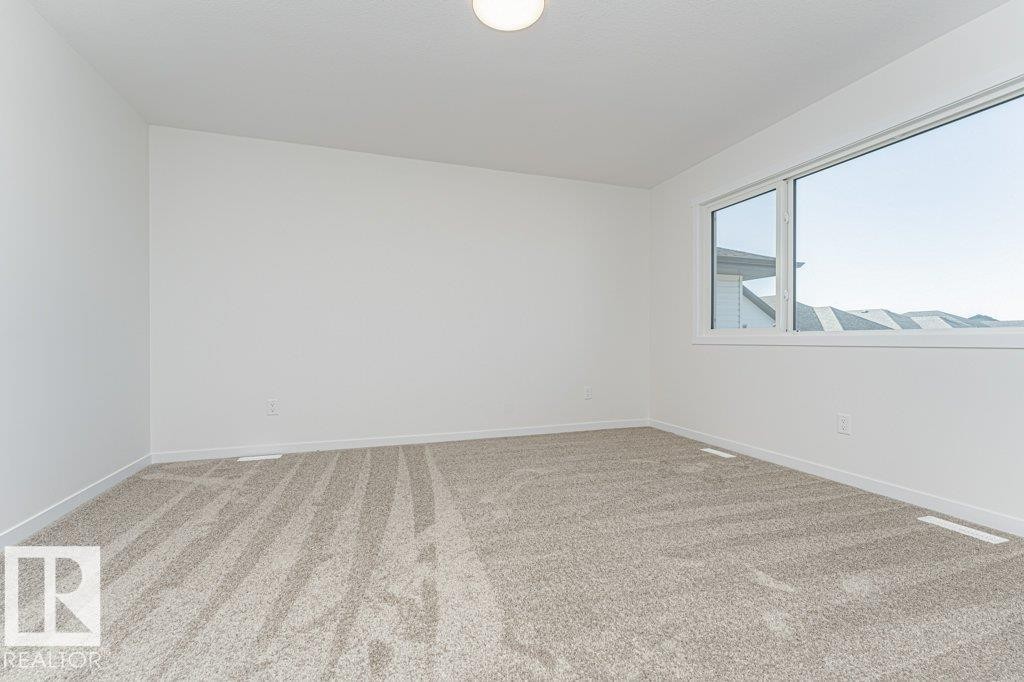 Bright room featuring a large window, light-toned carpet, white walls, and a ceiling-mounted light fixture - 6271 180 Avenue Nw, Edmonton, AB