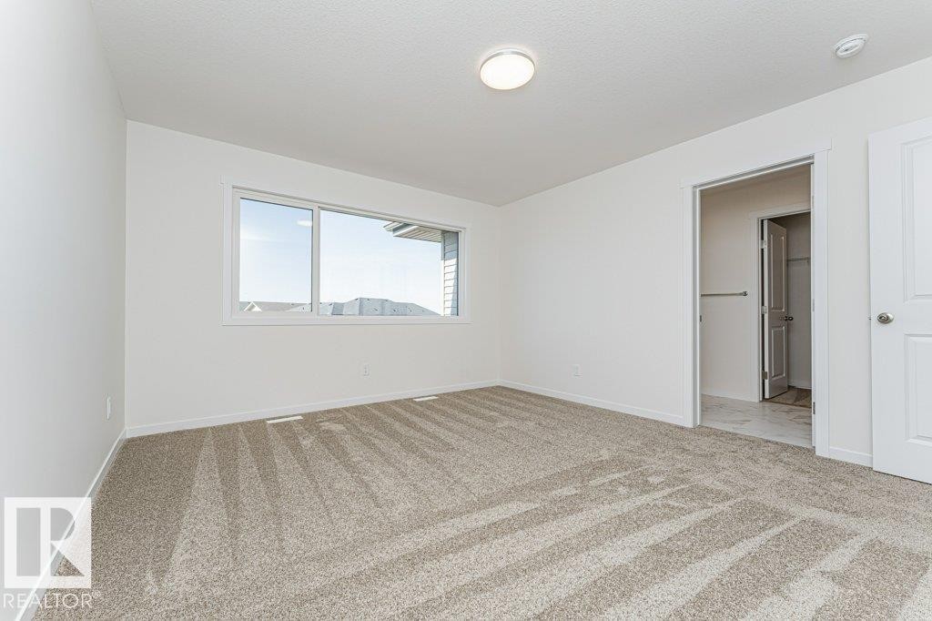 Spacious room with plush carpet flooring, a large window, and an overhead light fixture - 6271 180 Avenue Nw, Edmonton, AB