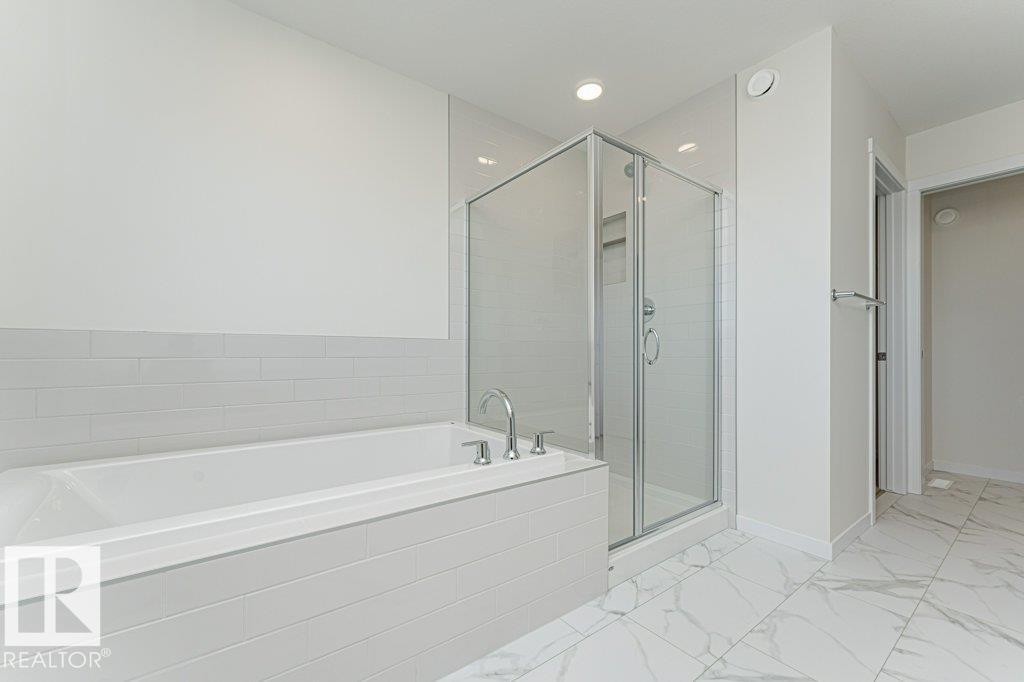 Contemporary bathroom featuring a built-in tub with deck-mounted fixtures, a glass-enclosed shower, white subway tile wainscoting, white walls, and white-patterned floor tiling - 6271 180 Avenue Nw, Edmonton, AB