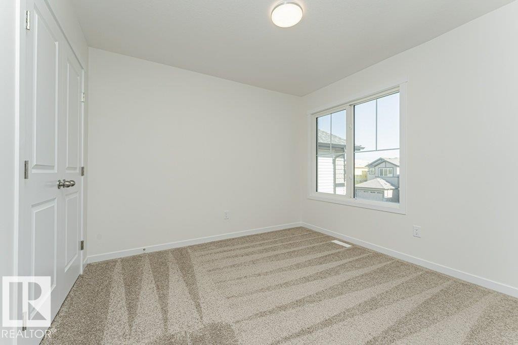 Bright room featuring a large window, neutral carpeting, white trim, and a flush mount ceiling light fixture - 6271 180 Avenue Nw, Edmonton, AB