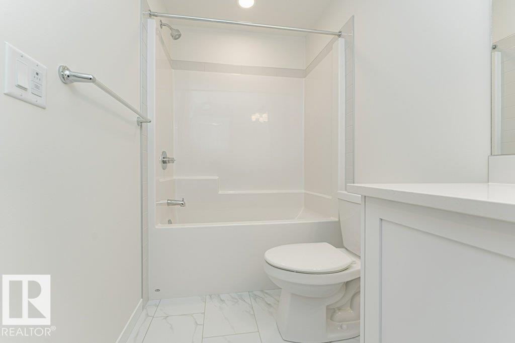 Bathroom featuring a white tub/shower combination, white toilet, white vanity with a light-toned countertop, and light-toned tile flooring - 6271 180 Avenue Nw, Edmonton, AB