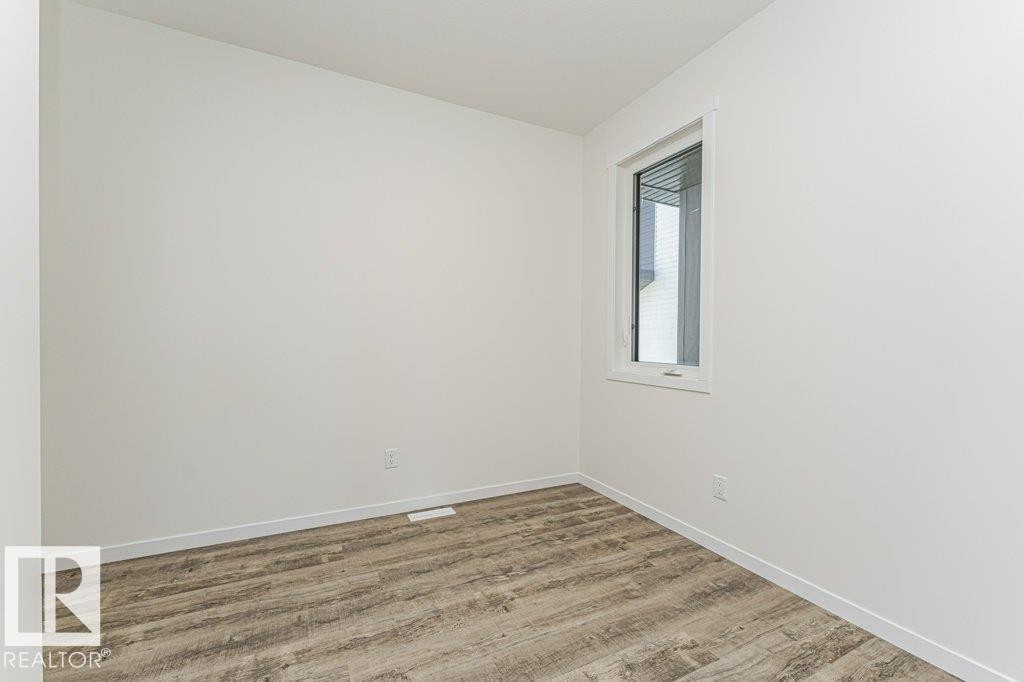 Bright room featuring white walls, white trim, a single window, and wood-finish flooring - 6271 180 Avenue Nw, Edmonton, AB