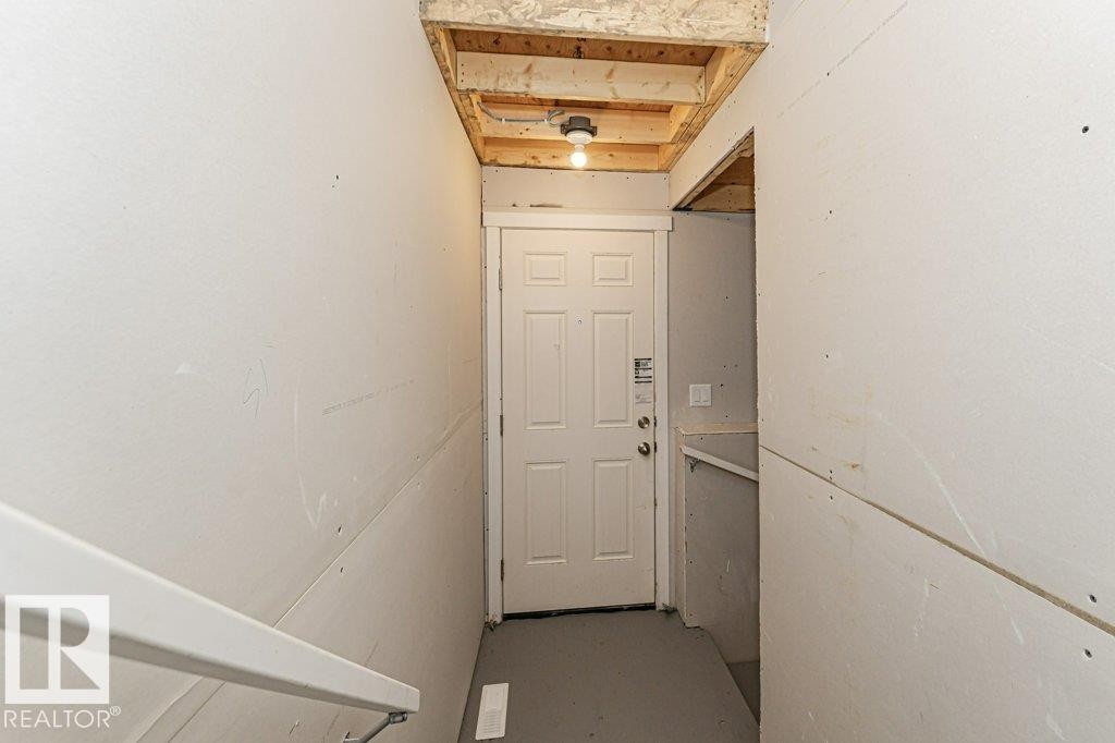 Stairwell with white six-panel door, light gray flooring, and wood beam ceiling - 6271 180 Avenue Nw, Edmonton, AB