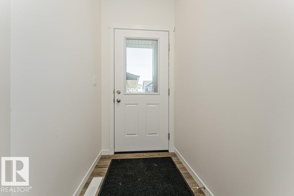 Entryway featuring a white paneled door with an upper glass insert, wood-finish flooring, and crisp white walls - 6271 180 Avenue Nw, Edmonton, AB