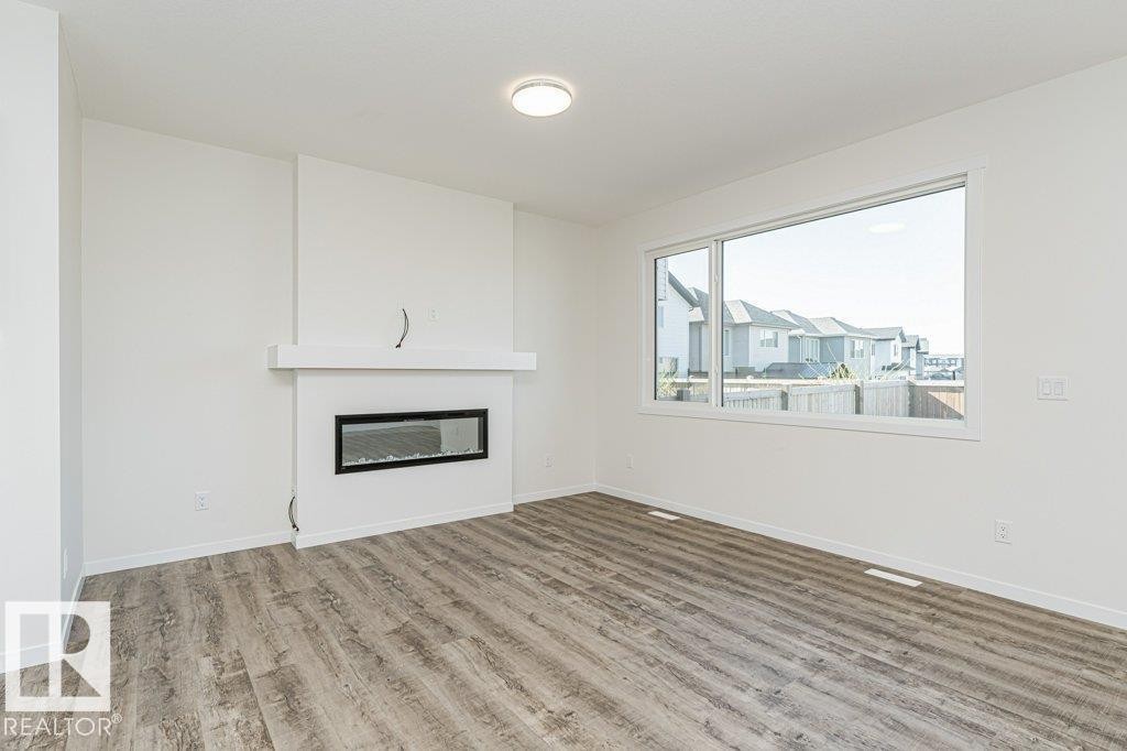 Spacious interior featuring wood-finish flooring, a contemporary fireplace with mantel, a large window, and recessed lighting - 6271 180 Avenue Nw, Edmonton, AB