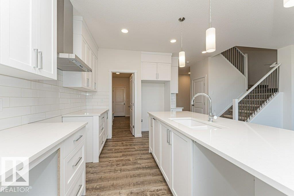 Modern kitchen featuring white shaker cabinetry, white subway tile backsplash, white countertops, wood-finish flooring, and a stainless steel range hood - 6271 180 Avenue Nw, Edmonton, AB