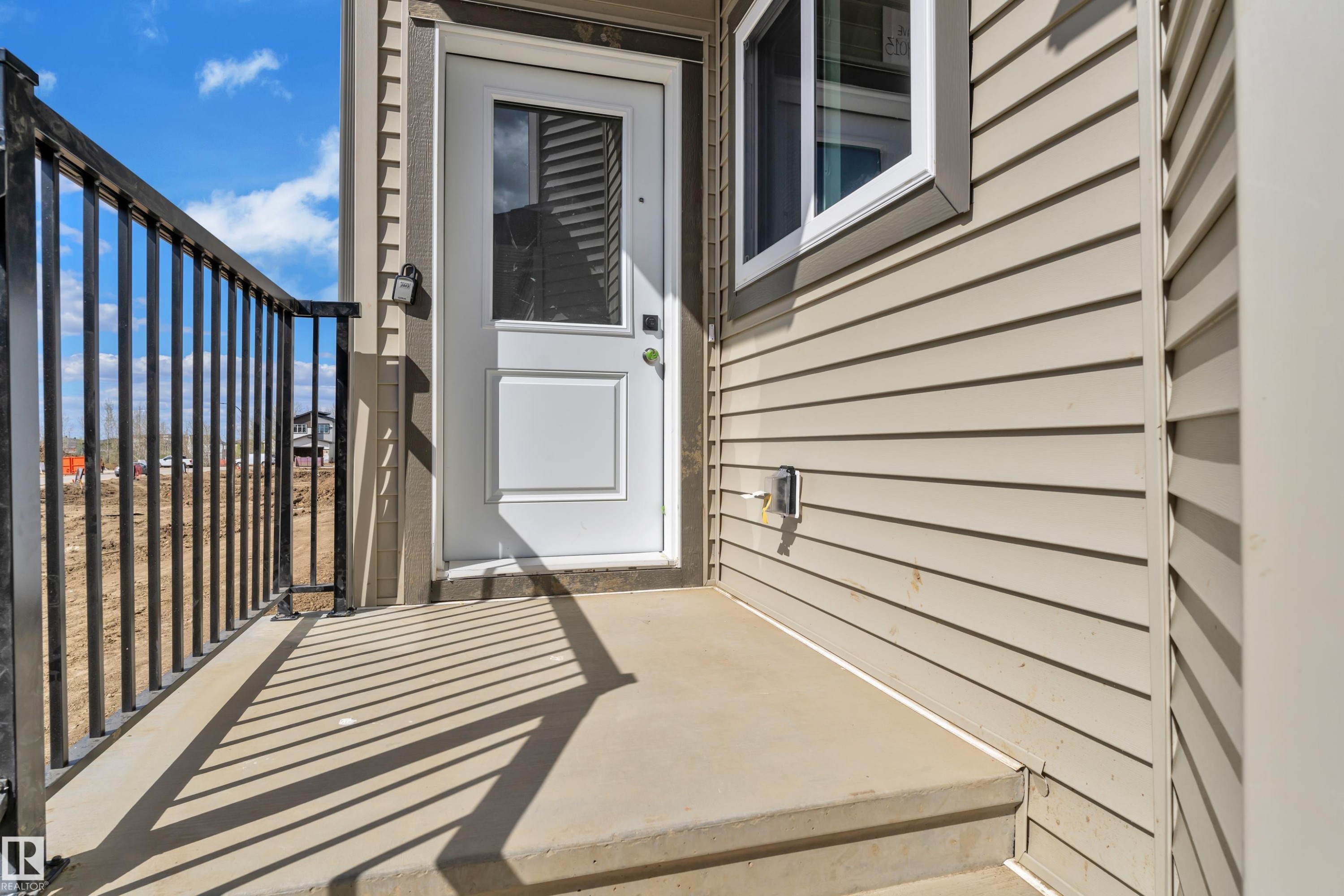 Entryway featuring a white door with upper glass panel, concrete porch, and black metal railing - 3116 8 Avenue, Edmonton, AB
