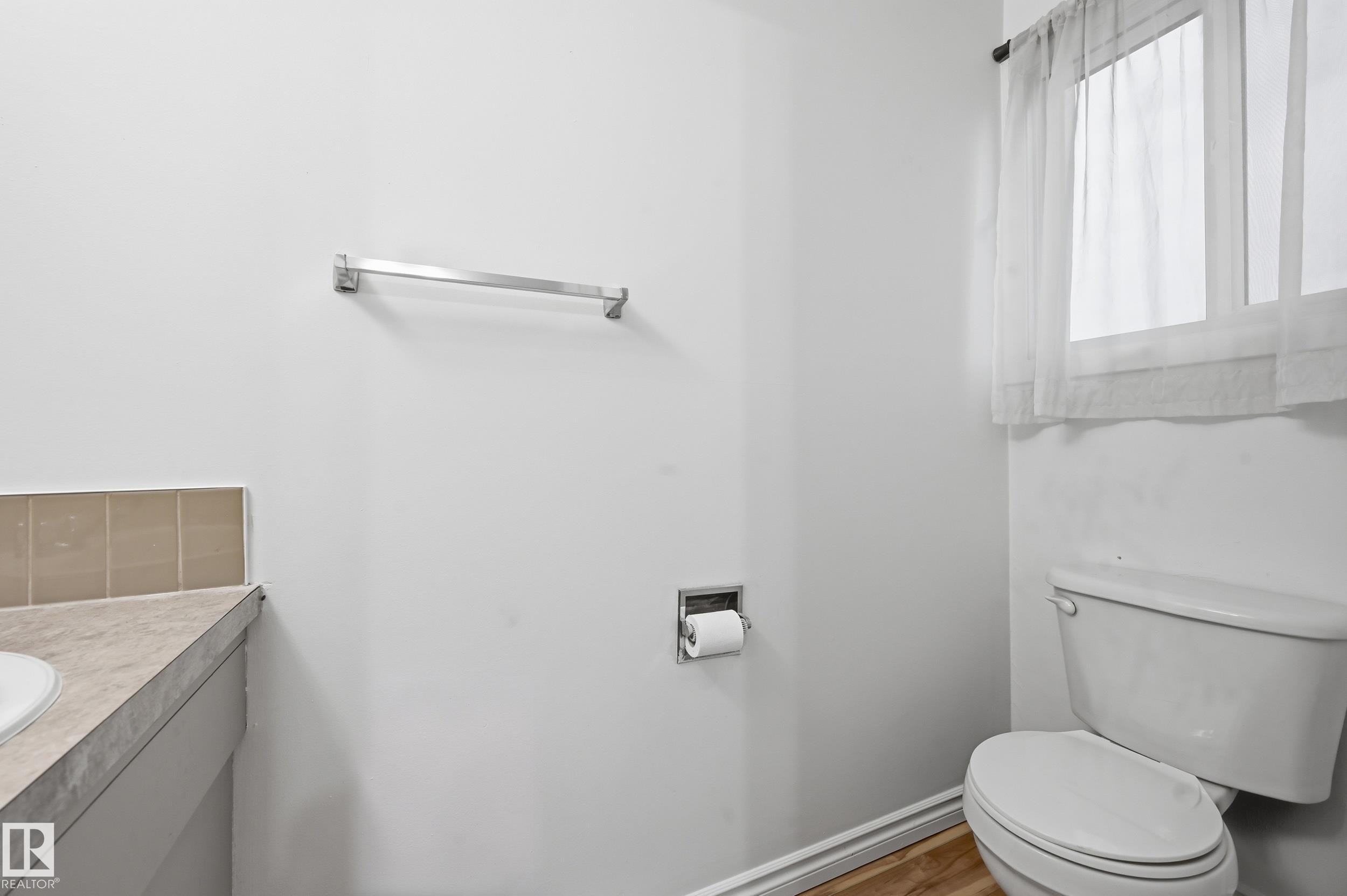 Bathroom featuring a window with sheer curtains, a white toilet, and a vanity with a light-colored countertop and tiled backsplash - 13903 87 Street, Edmonton, AB - Indoor Photo Showing Bathroom