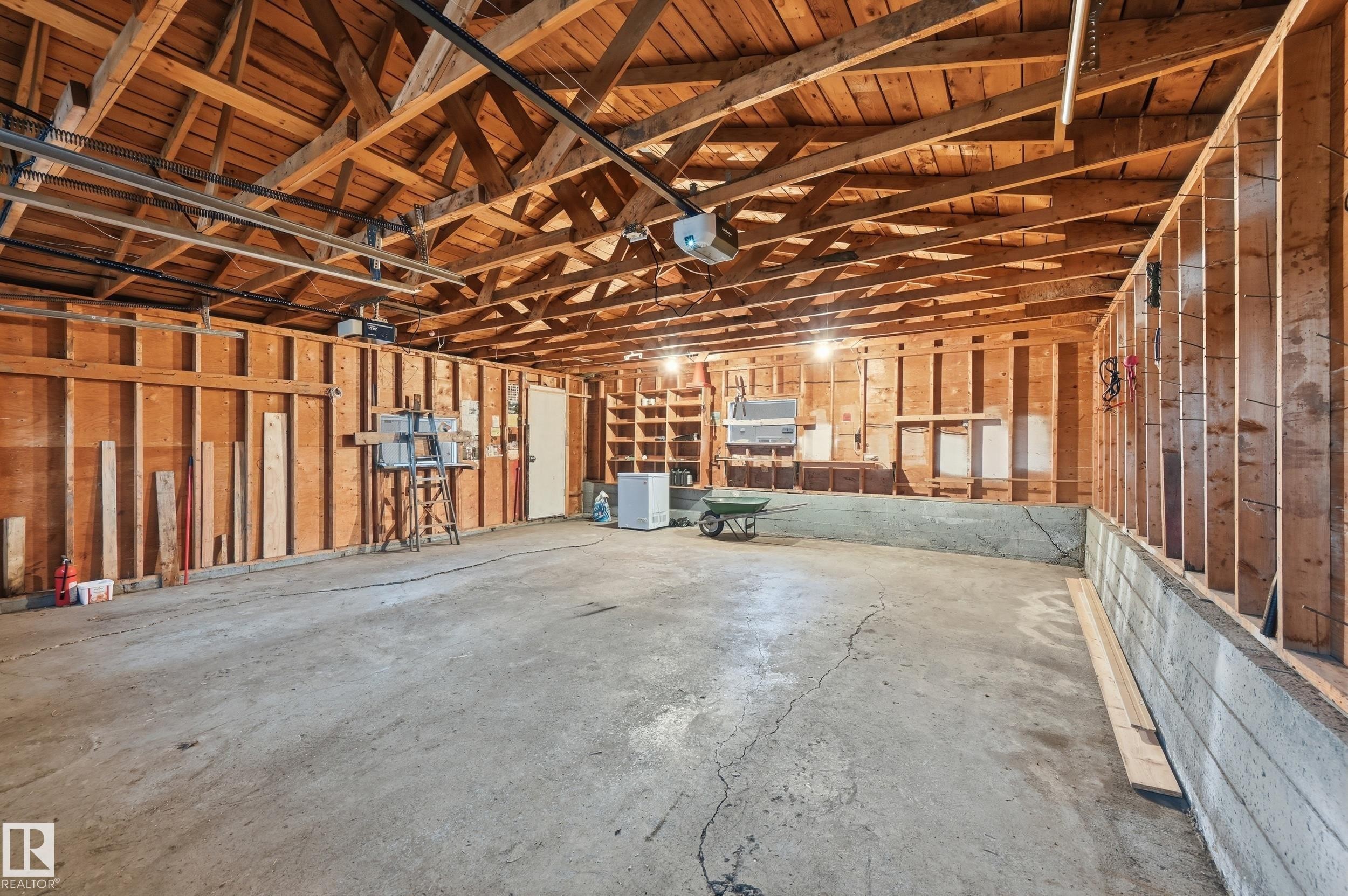 Spacious garage with exposed wood beam ceiling, concrete flooring, and built-in shelving - 13903 87 Street, Edmonton, AB - Indoor Photo Showing Garage