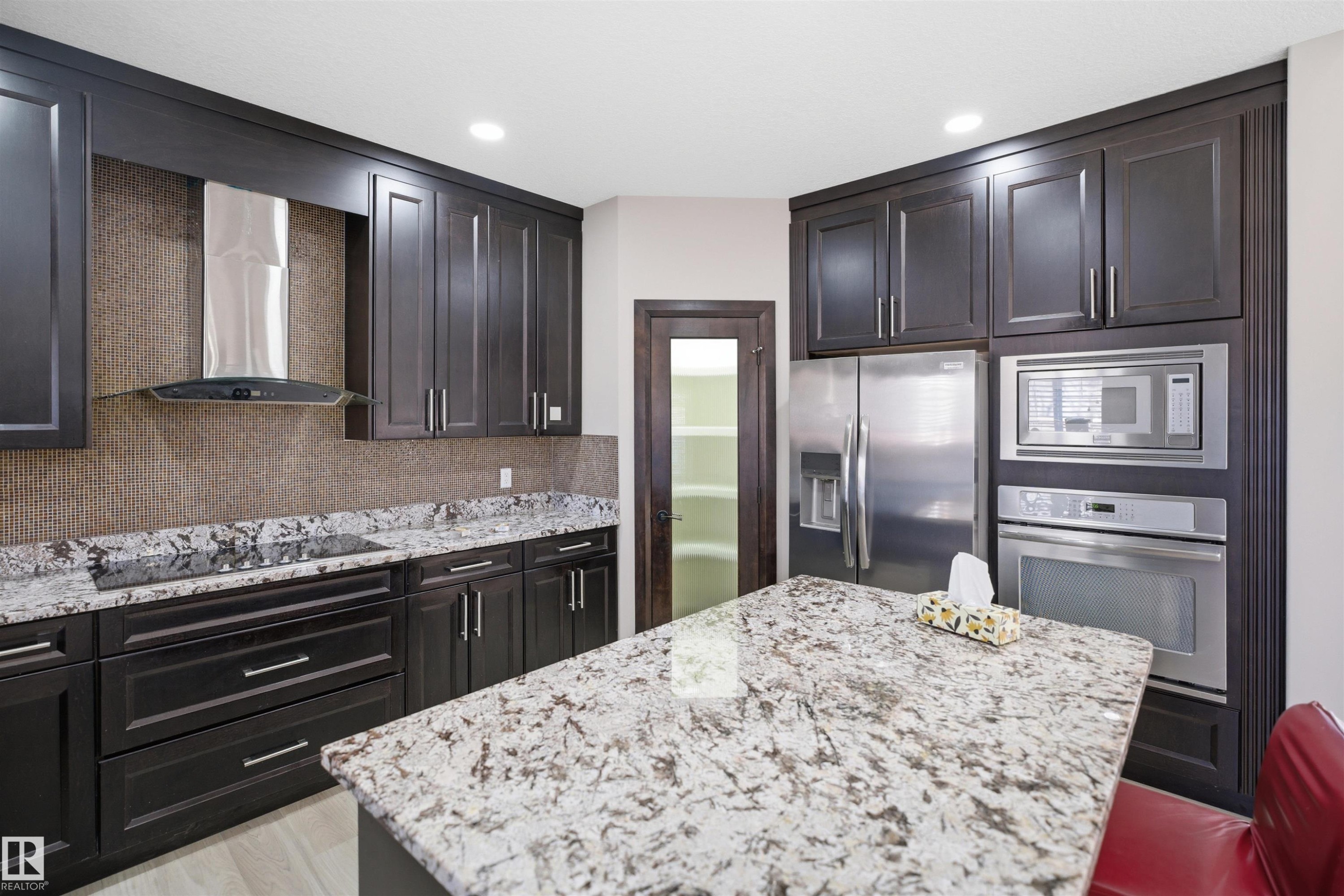 Kitchen featuring dark wood cabinetry, a granite island countertop, and integrated stainless steel appliances including a refrigerator, microwave, and oven - 2256 Cameron Ravine Court, Edmonton, AB - Indoor Photo Showing Kitchen With Stainless Steel Kitchen With Upgraded Kitchen