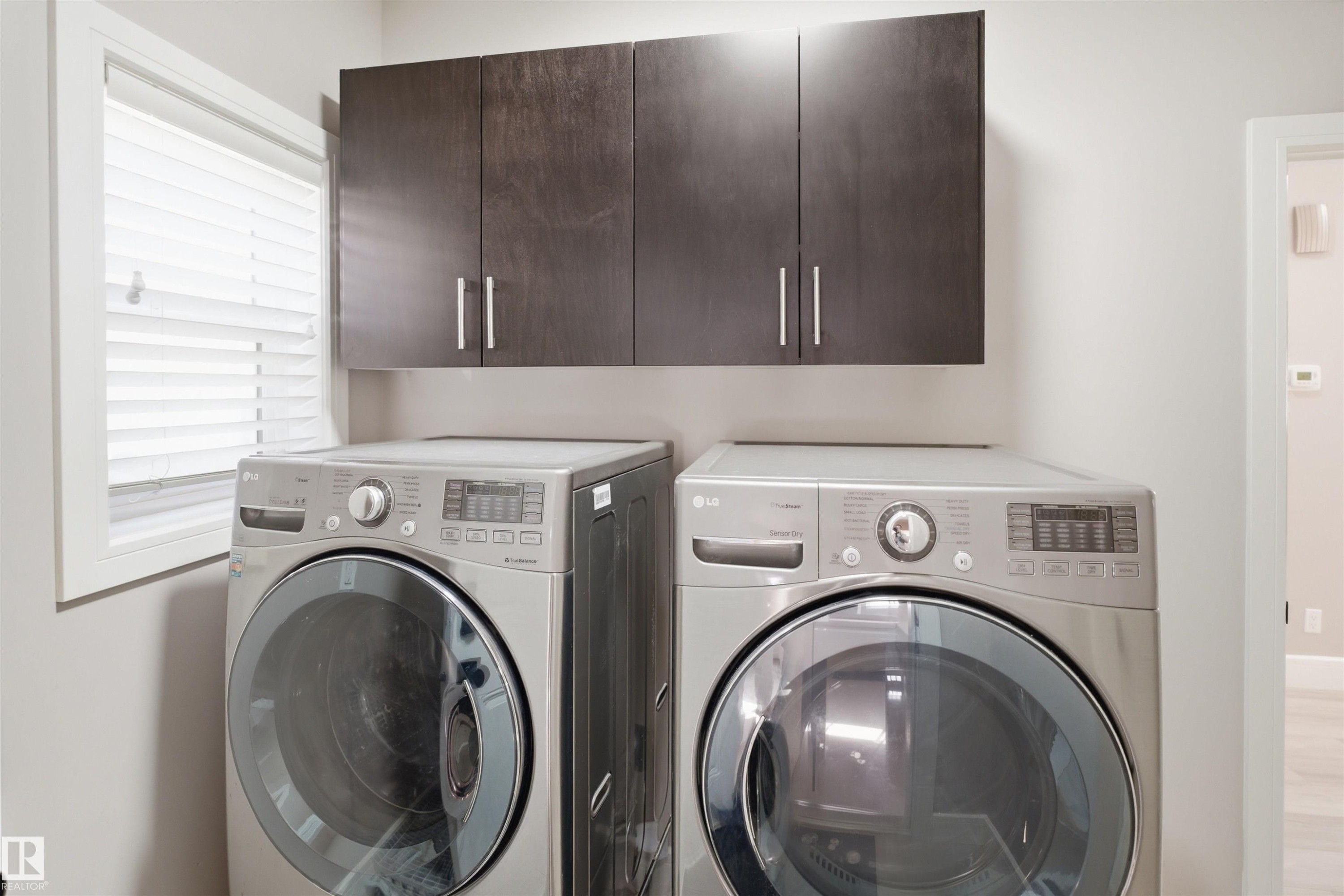 Laundry area featuring a side-by-side washer and dryer, dark wood-finish cabinetry with silver hardware, and a window with white blinds - 2256 Cameron Ravine Court, Edmonton, AB - Indoor Photo Showing Laundry Room
