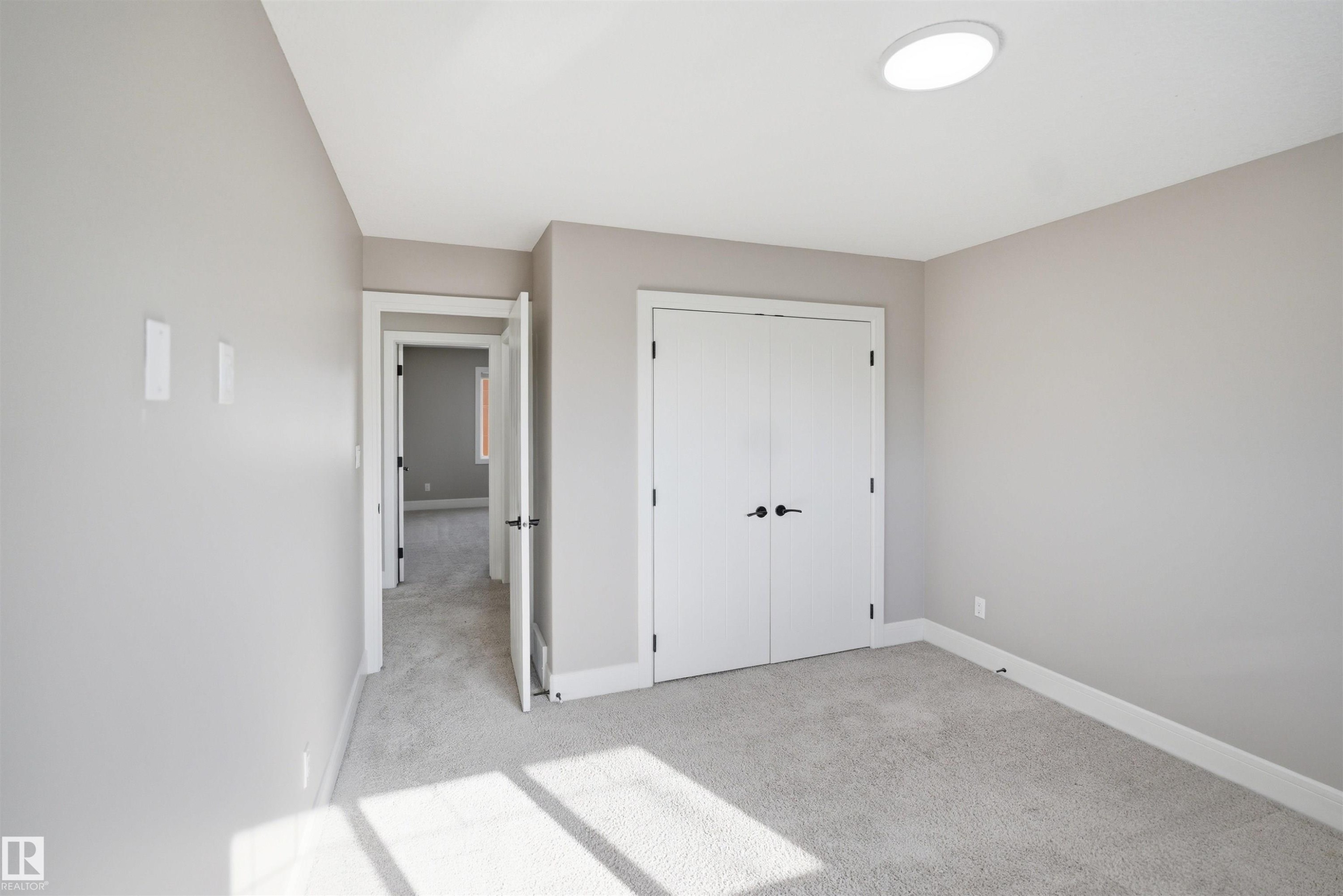 Neutral toned room featuring plush carpet flooring, a ceiling-mounted light fixture, white baseboards, and a double-door closet with dark hardware - 2256 Cameron Ravine Court, Edmonton, AB - Indoor Photo Showing Other Room