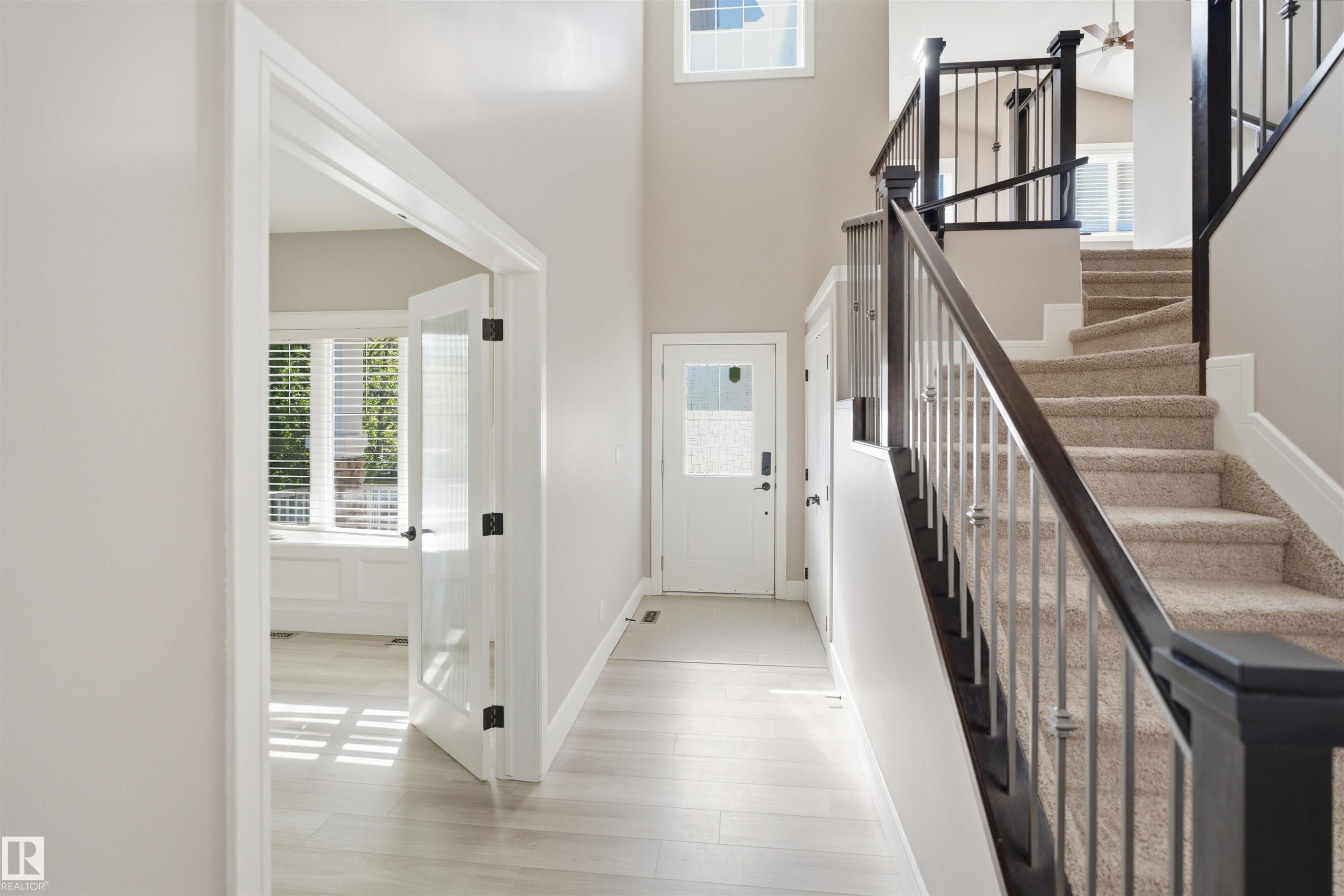 Grand entry hall featuring light wood-finish flooring, a carpeted staircase with dark wood newel posts and railings, and metal balusters - 2256 Cameron Ravine Court, Edmonton, AB - Indoor Photo Showing Other Room