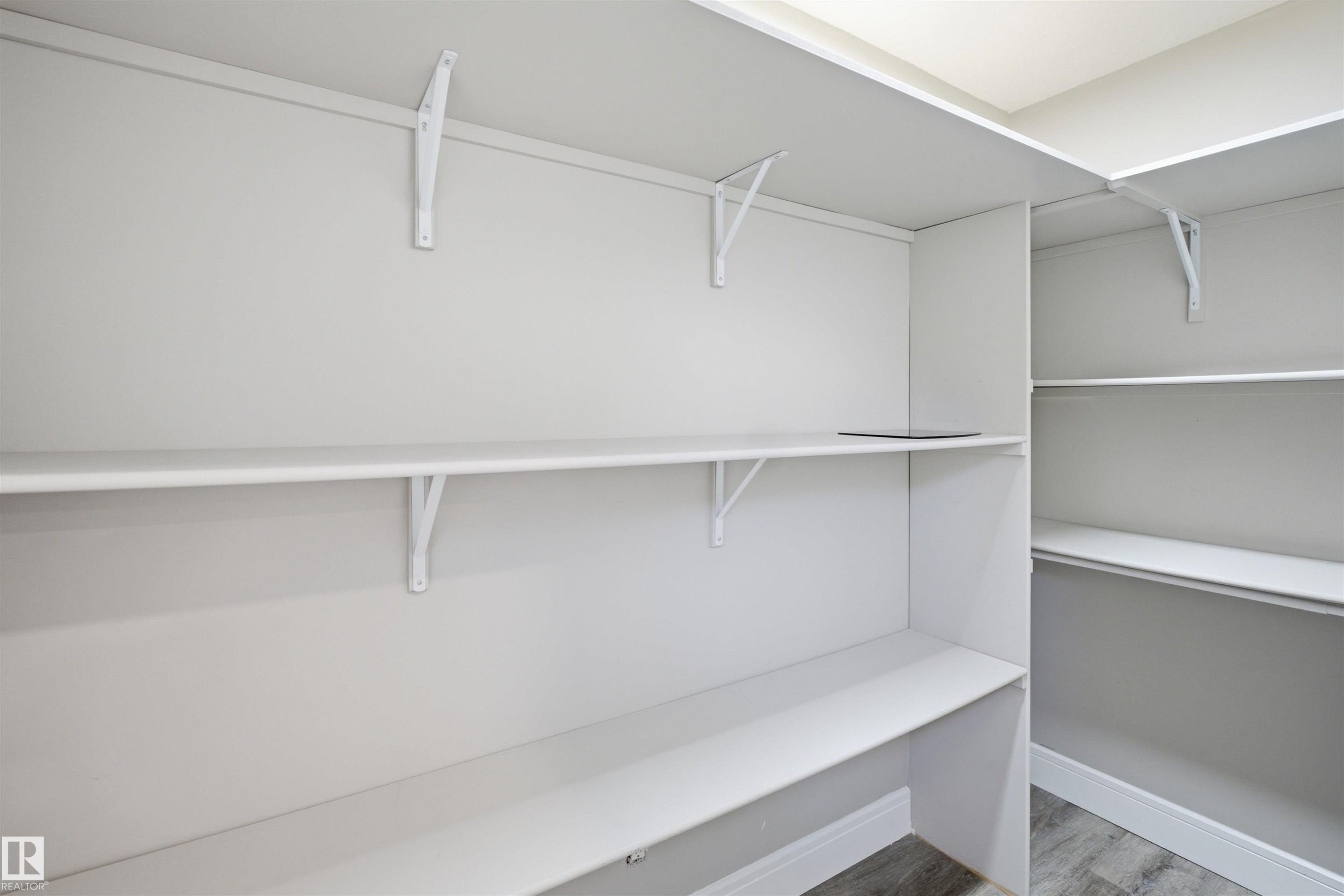 Walk-in closet featuring white built-in shelving, white walls, and wood-finish flooring - 2256 Cameron Ravine Court, Edmonton, AB - Indoor With Storage