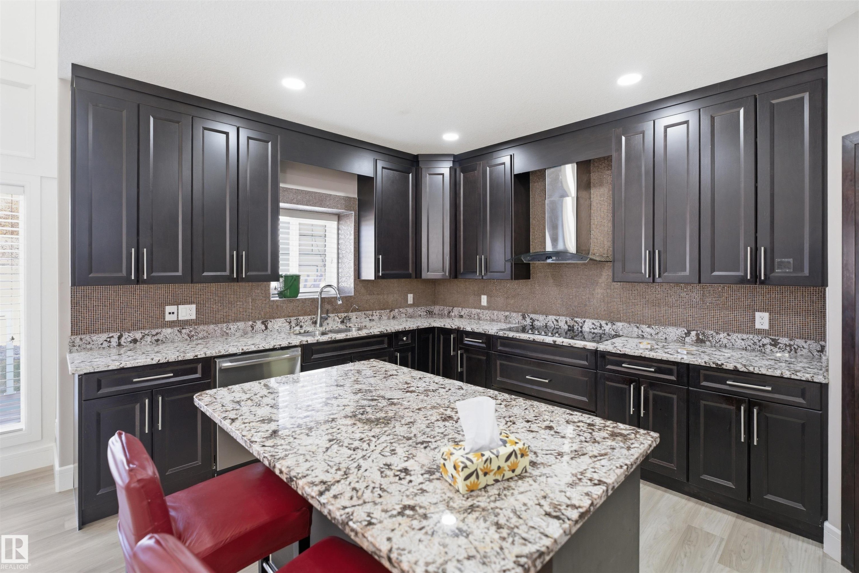 Contemporary kitchen featuring dark wood cabinetry, light granite countertops, a built-in stainless steel dishwasher, a sleek range hood, and recessed lighting - 2256 Cameron Ravine Court, Edmonton, AB - Indoor Photo Showing Kitchen With Upgraded Kitchen