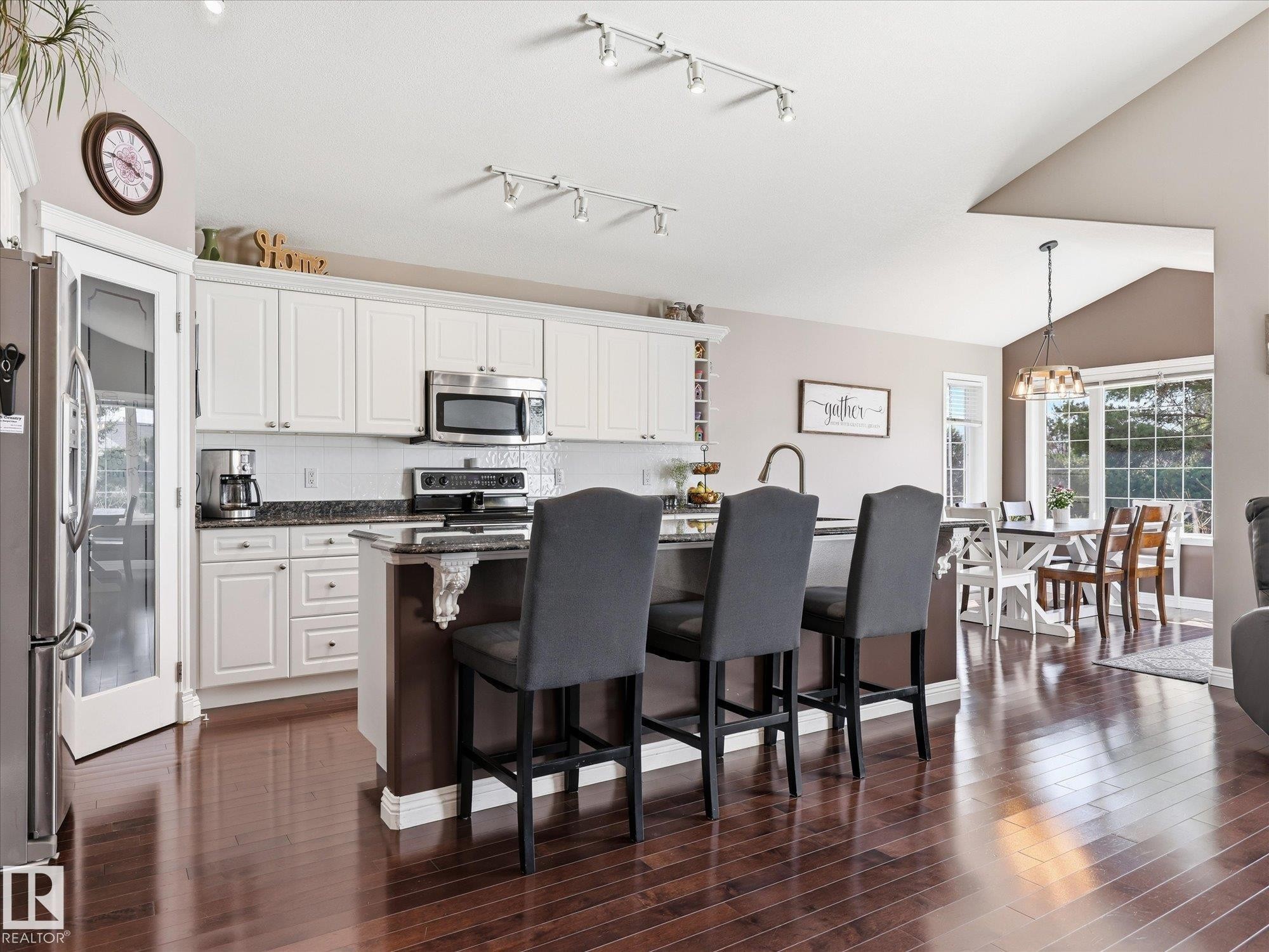 Open-concept kitchen featuring white cabinetry, stainless steel appliances, dark wood-finish flooring, and a central island with countertop seating - 1340 Oakland Crescent, Devon, AB - Indoor