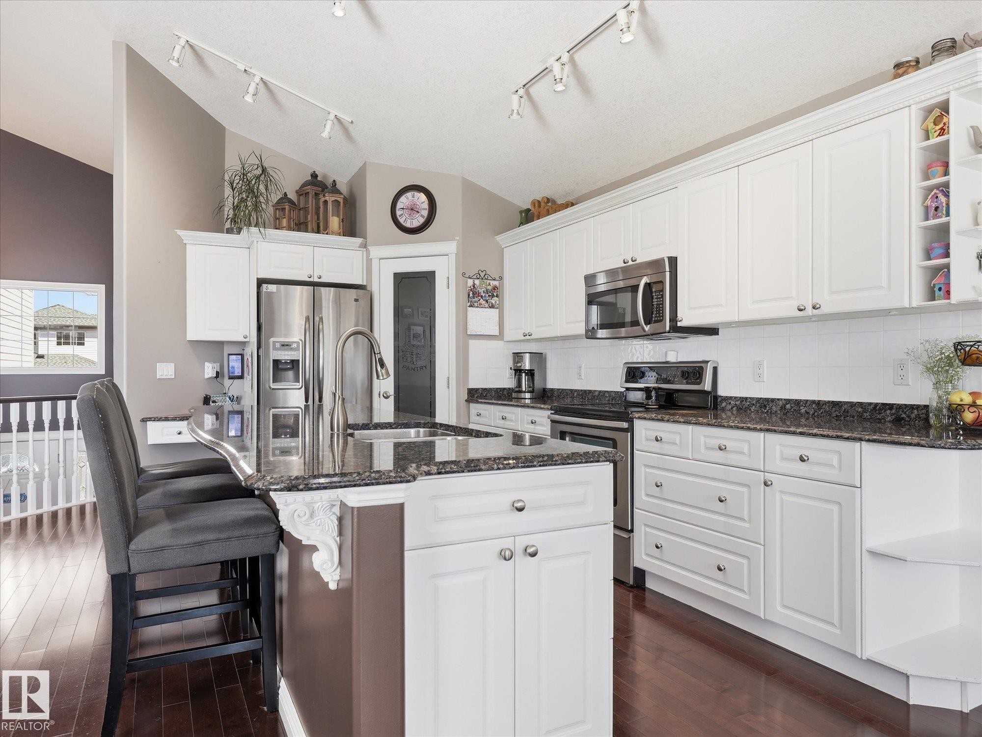 Kitchen featuring white cabinetry, dark wood-finish flooring, stainless steel appliances, granite countertops, and an island with bar seating - 1340 Oakland Crescent, Devon, AB - Indoor Photo Showing Kitchen With Upgraded Kitchen