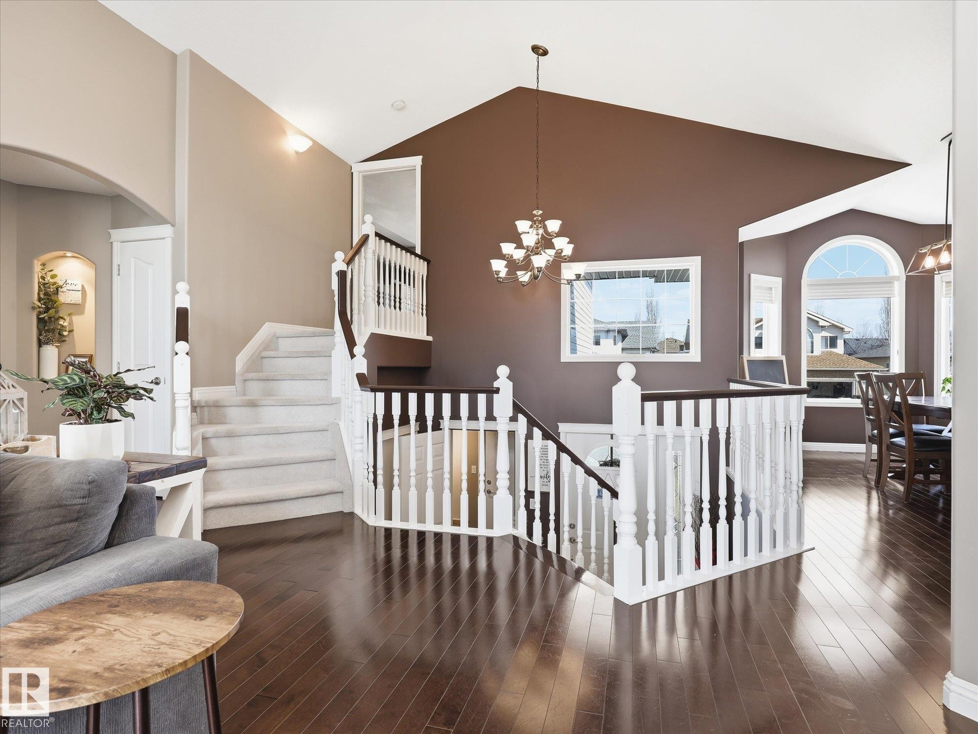 Hardwood-finish flooring extending through the main level, complemented by a grand staircase with white balusters and dark wood handrails - 1340 Oakland Crescent, Devon, AB - Indoor Photo Showing Other Room
