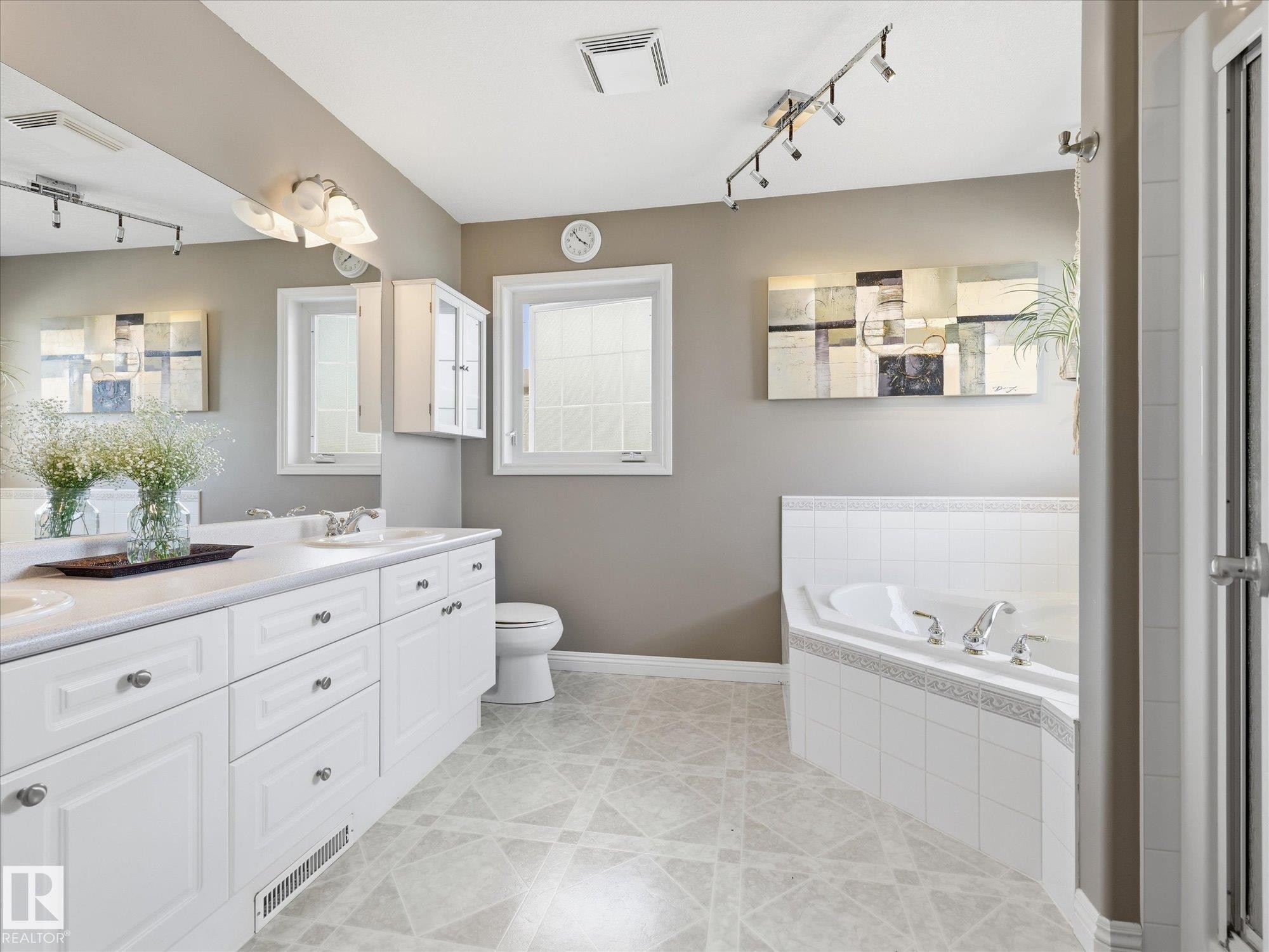 Spacious bathroom featuring a double vanity with white cabinetry, an integrated soaking tub with tiled surround, and patterned floor tiling - 1340 Oakland Crescent, Devon, AB - Indoor Photo Showing Bathroom