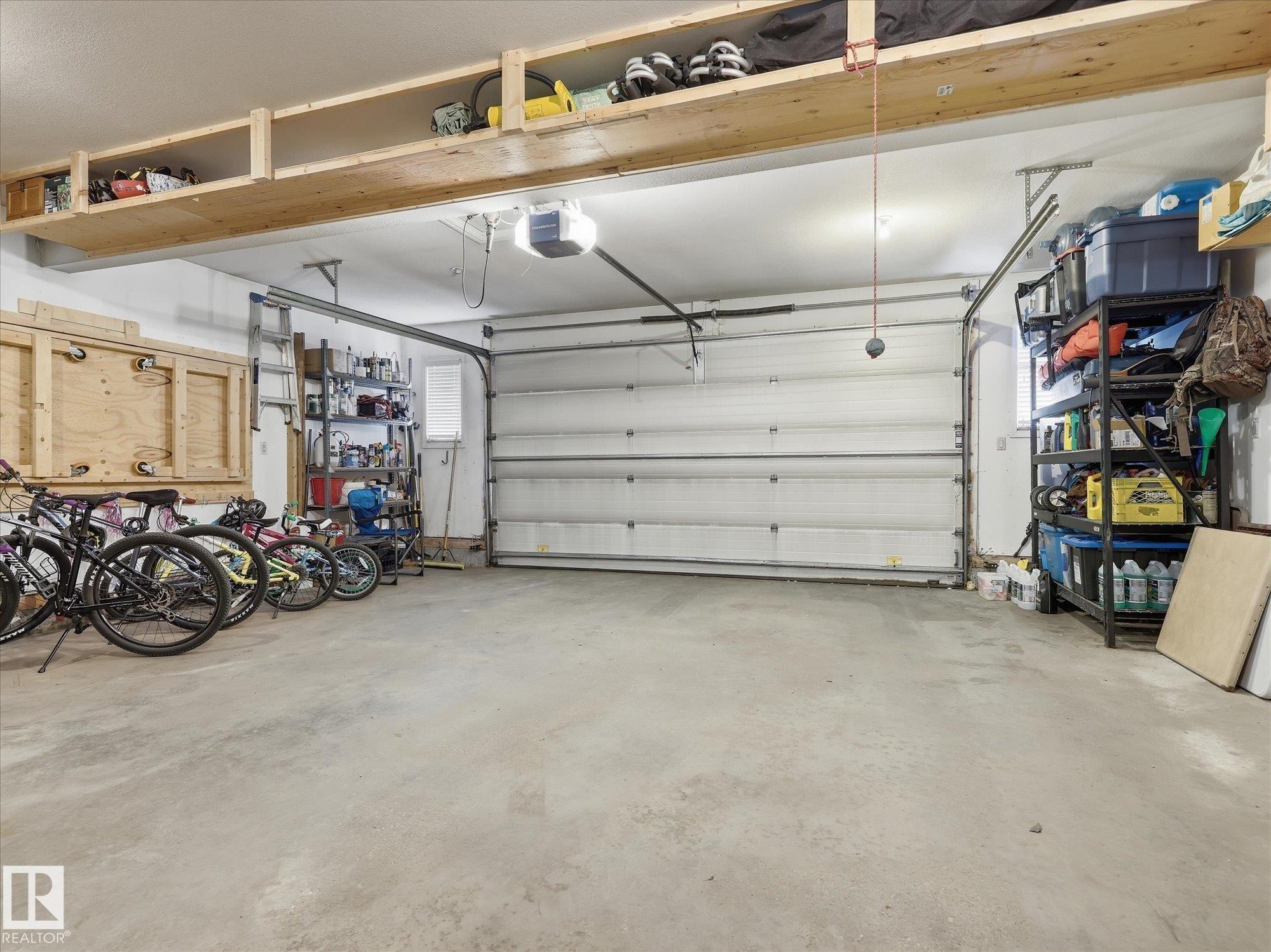 Concrete floor garage featuring an overhead garage door, built-in wooden shelving, and a built-in workbench - 1340 Oakland Crescent, Devon, AB - Indoor Photo Showing Garage