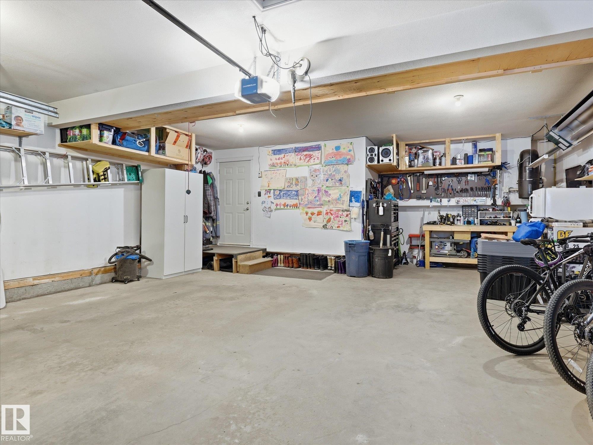 Spacious garage featuring a concrete floor, built-in overhead shelving, a utility door, an integrated workbench, and a pegboard tool organization system - 1340 Oakland Crescent, Devon, AB - Indoor Photo Showing Garage