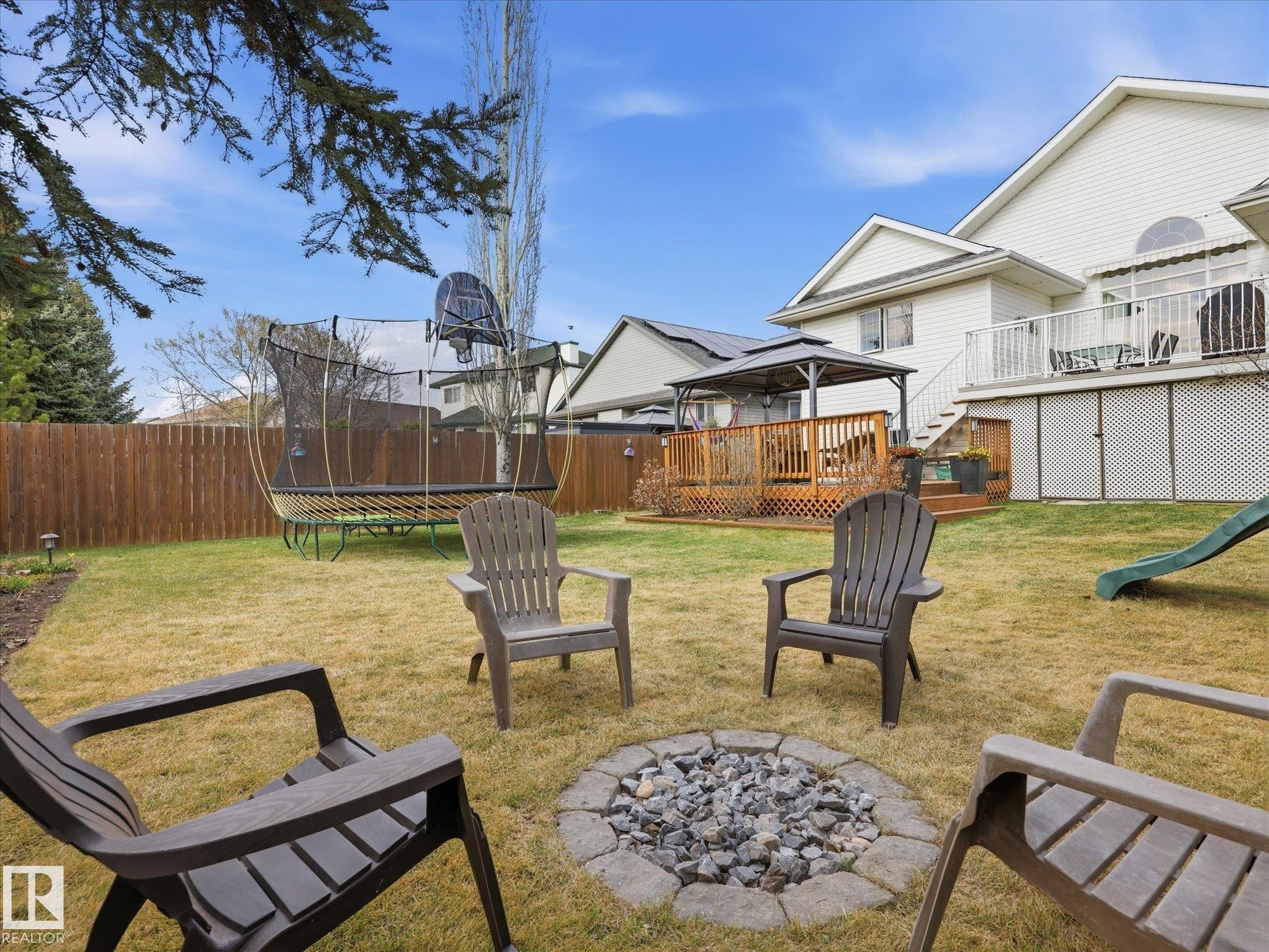 Expansive backyard featuring a stone-ringed fire pit, wood privacy fencing, a multi-level wood deck with a gazebo, and a secondary white deck with railings - 1340 Oakland Crescent, Devon, AB - Outdoor With Deck Patio Veranda With Backyard