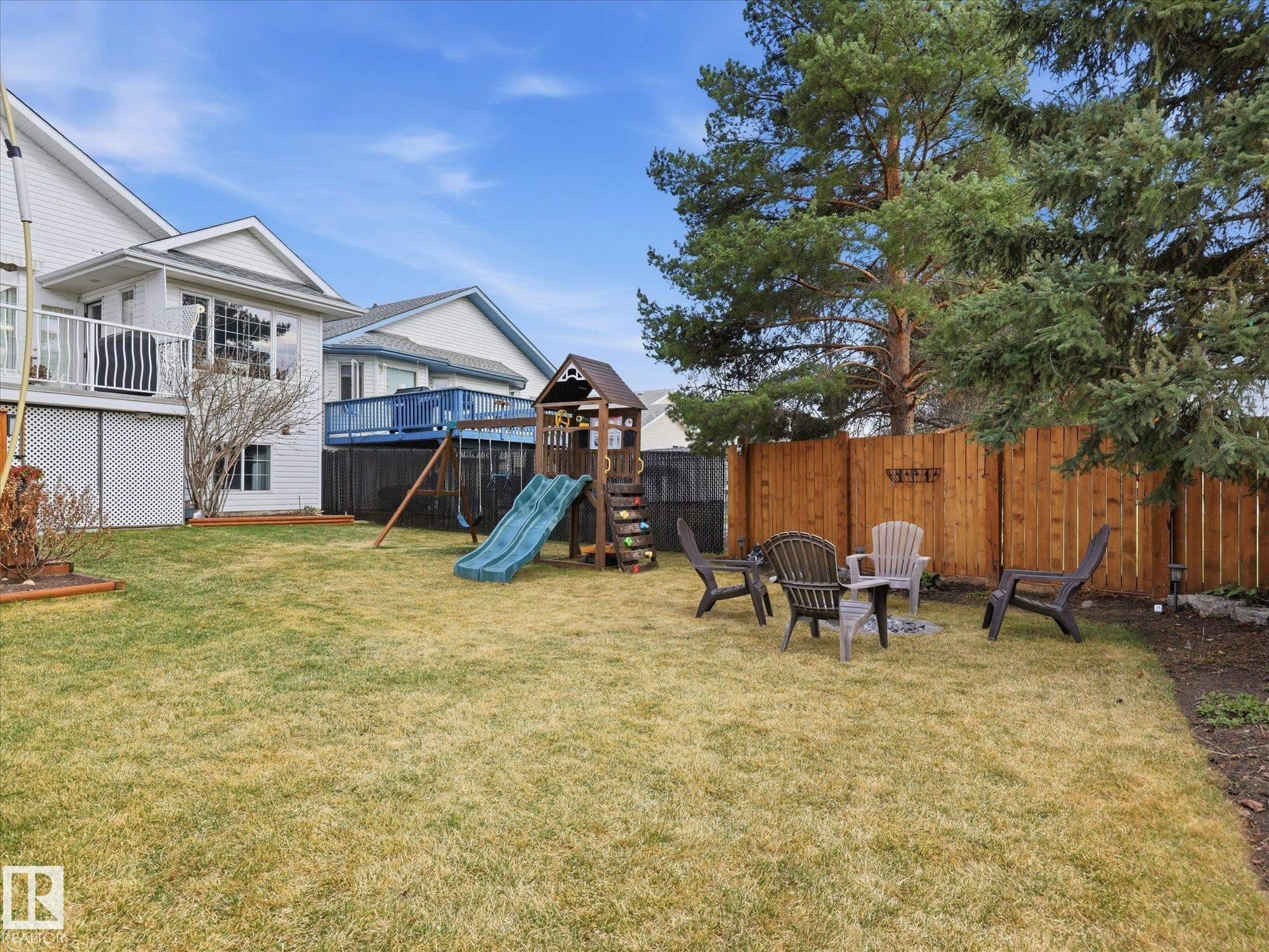 Spacious backyard featuring a manicured lawn, a wooden privacy fence, and mature evergreen trees - 1340 Oakland Crescent, Devon, AB - Outdoor With Deck Patio Veranda