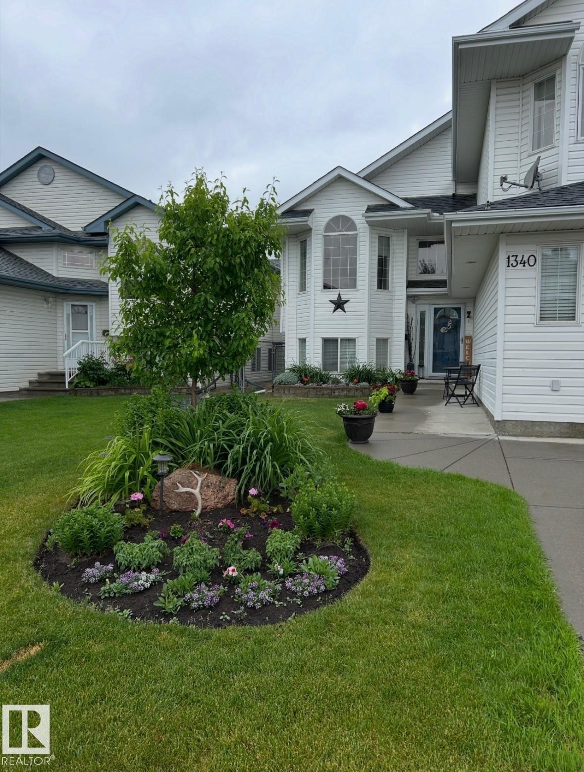 White siding exterior with a prominent arched window, established front landscaping, a paved walkway, and a manicured lawn - 1340 Oakland Crescent, Devon, AB - Outdoor With Facade