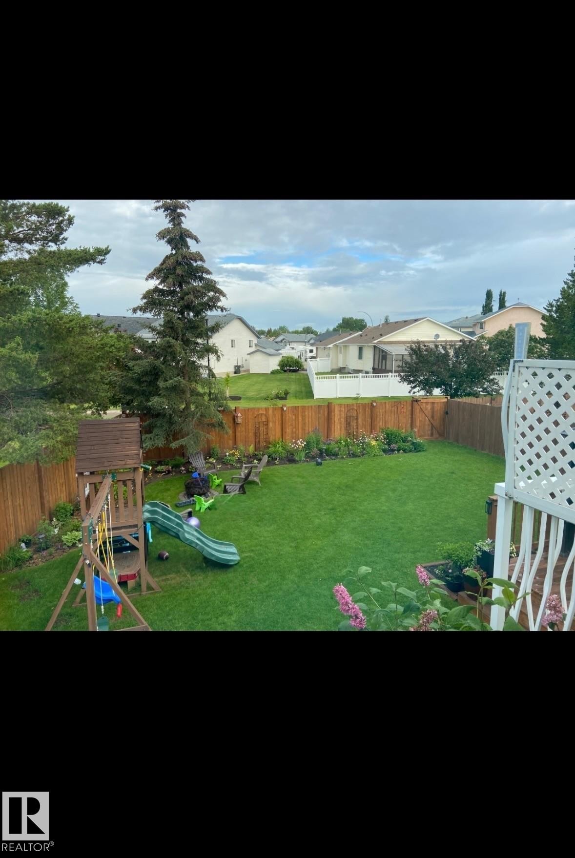 Expansive backyard featuring a lush lawn, wood privacy fencing, and established garden beds - 1340 Oakland Crescent, Devon, AB - Outdoor With Backyard