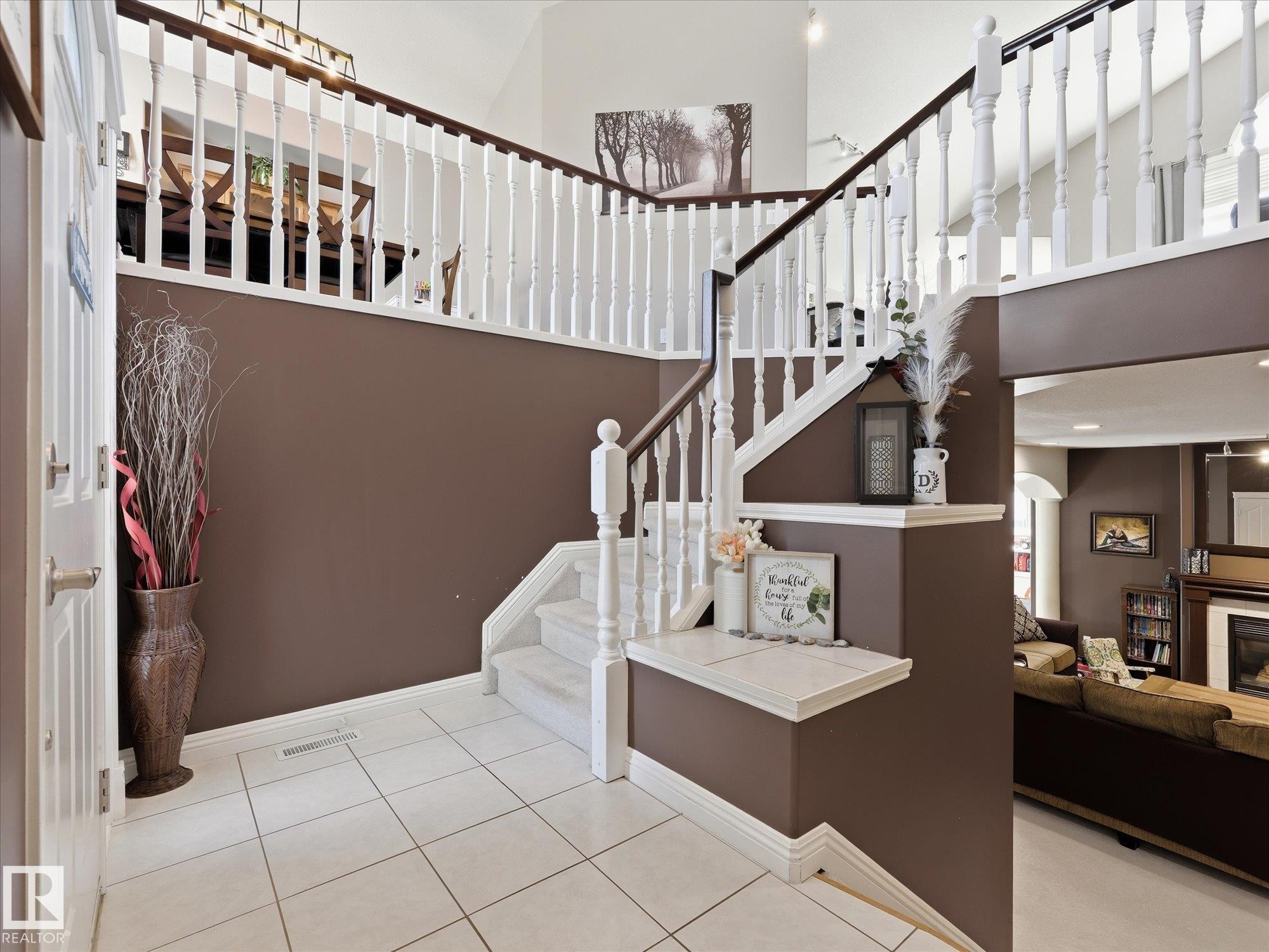 Two-story entryway featuring white tile flooring, a staircase with white spindles and dark wood banisters, and a landing with a built-in display shelf - 1340 Oakland Crescent, Devon, AB - Indoor Photo Showing Other Room