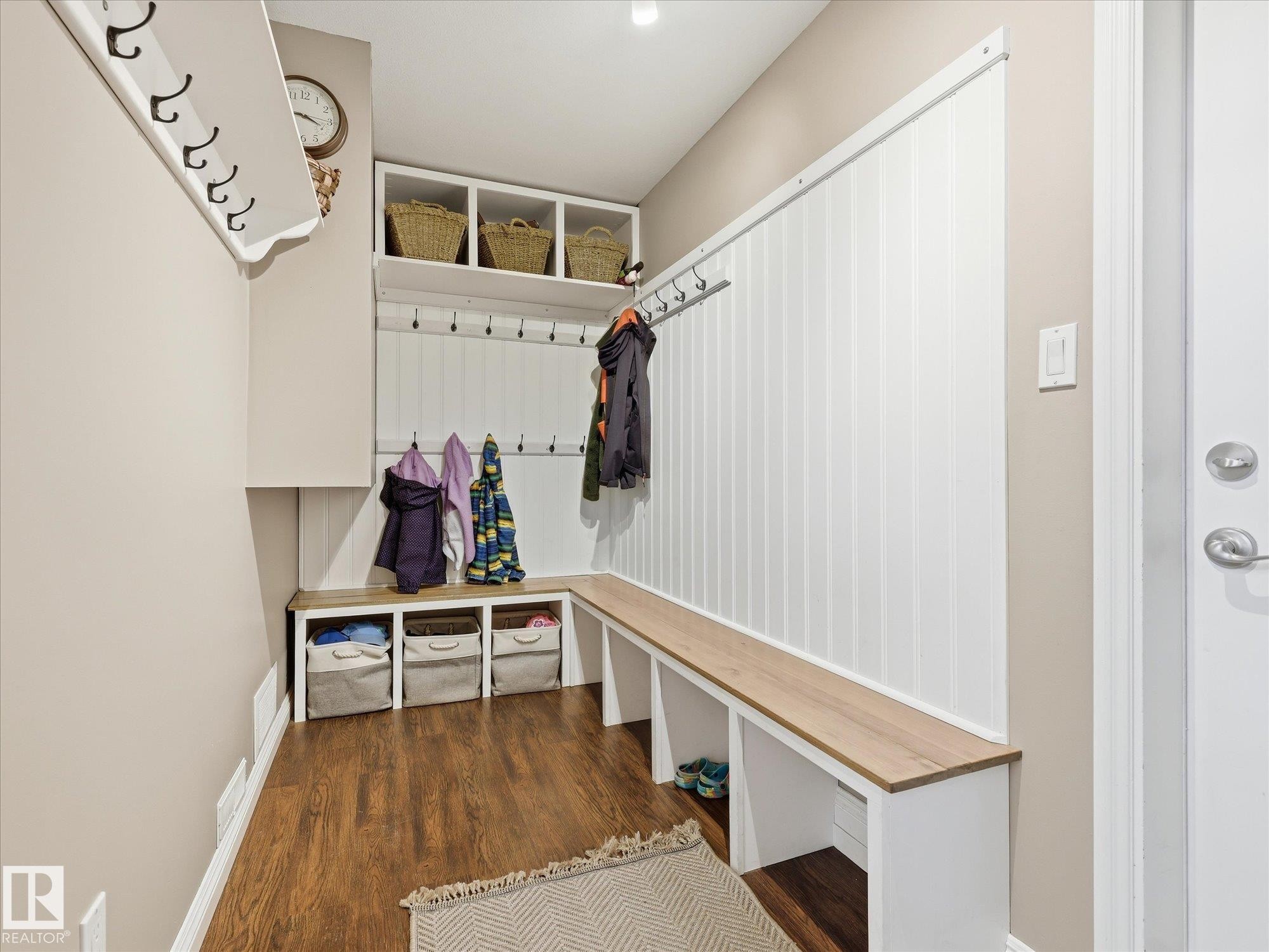 Entryway featuring built-in white cabinetry, wood-finish flooring, a wood-finish bench, and a white paneled accent wall with integrated coat hooks - 1340 Oakland Crescent, Devon, AB - Indoor Photo Showing Other Room