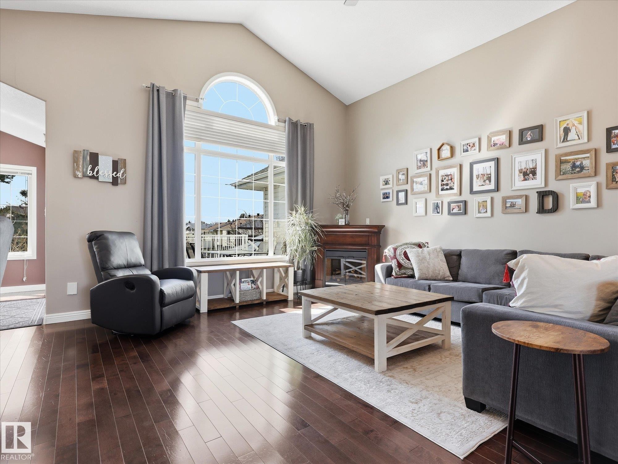 Spacious living area featuring high vaulted ceilings, rich wood-finish flooring, and a prominent fireplace with a wood mantel - 1340 Oakland Crescent, Devon, AB - Indoor Photo Showing Living Room